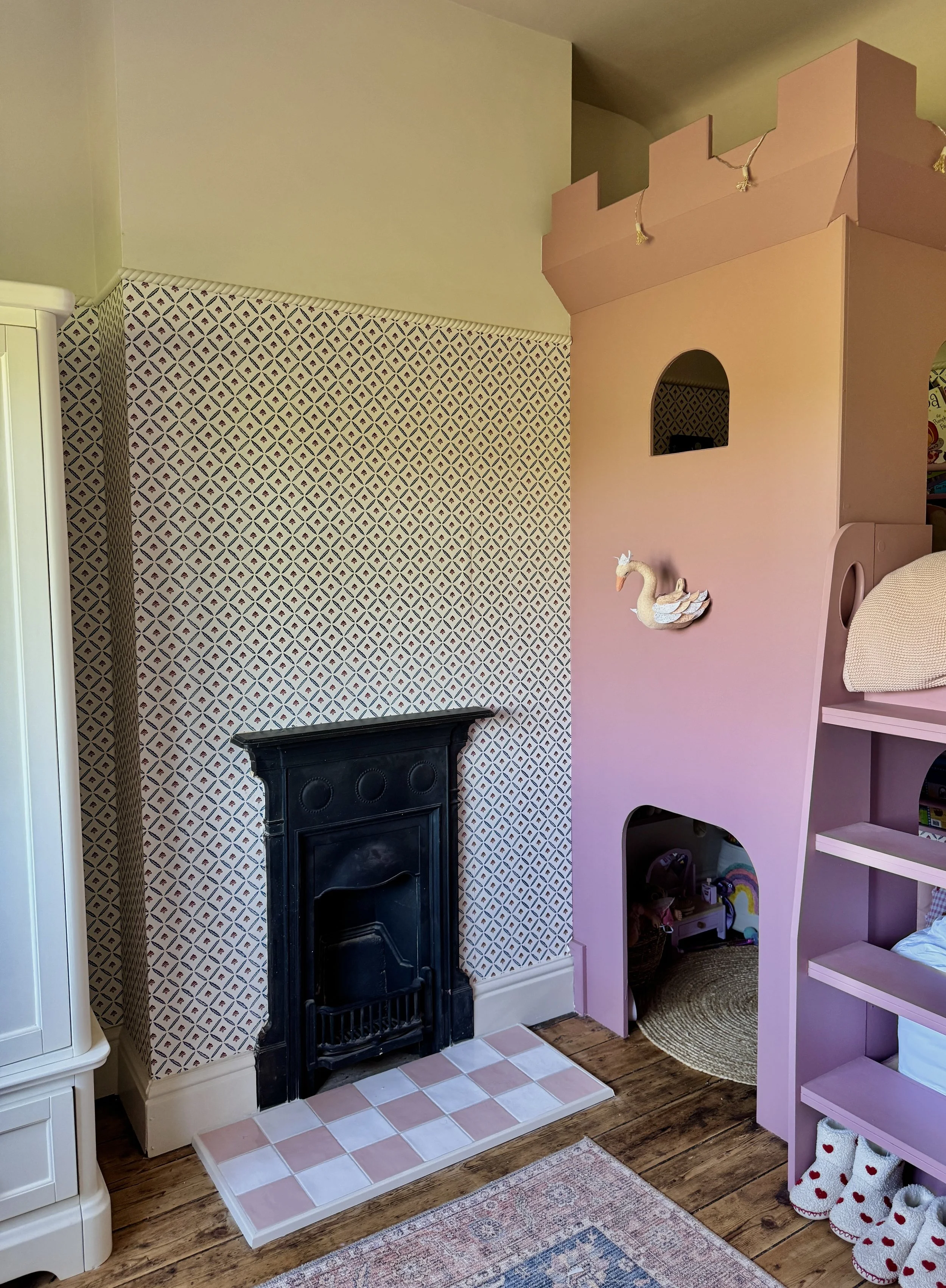 Children's bedroom featuring a bespoke playhouse bed, patterned wallpaper and original cast iron fireplace.