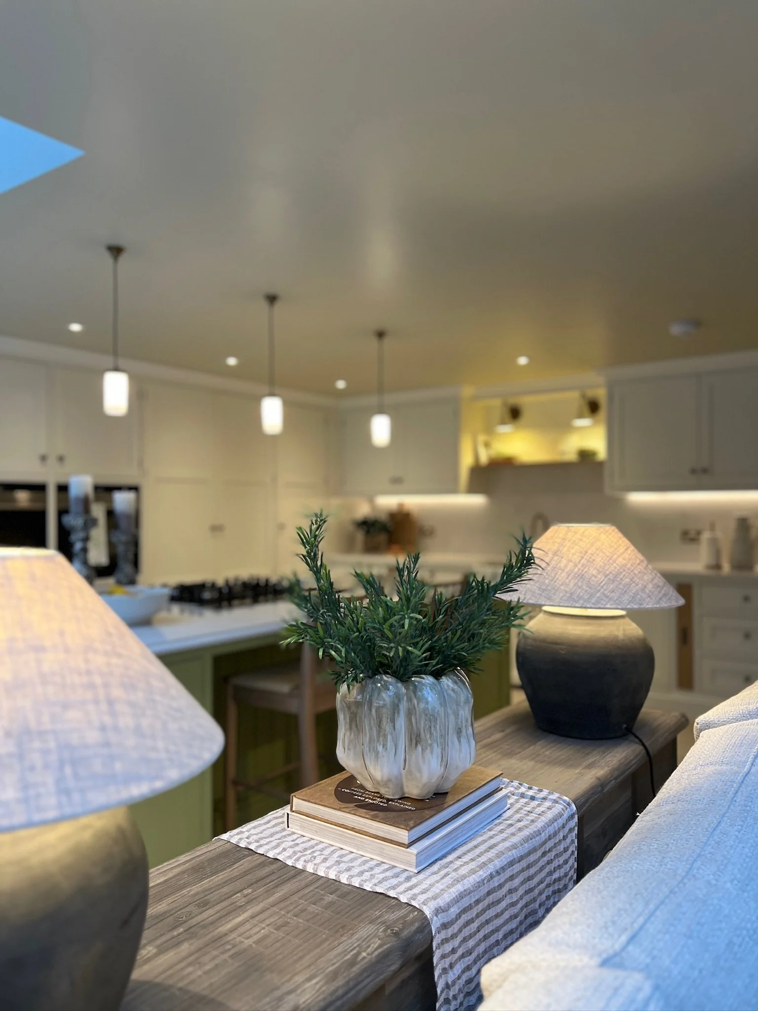 Styled console table with vintage ceramic lamps overlooking the bespoke open plan kitchen and living space in a contemporary West Midlands family home designed by Istigh Interiors.