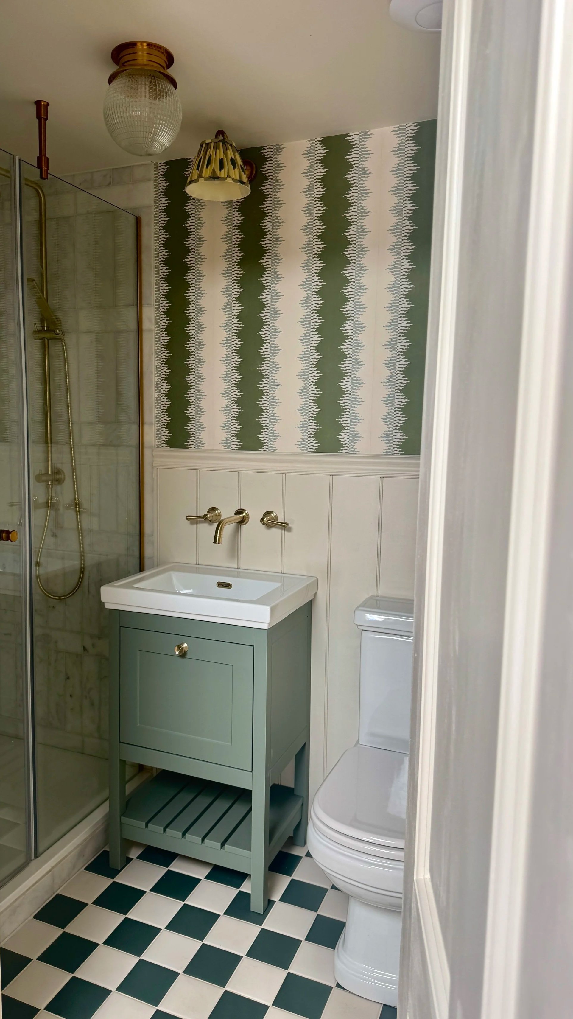 Shower room at Brook Cottage featuring checkerboard floor tiles and statement striped wallpaper designed by Istigh Interiors in Bridgnorth, Shropshire.