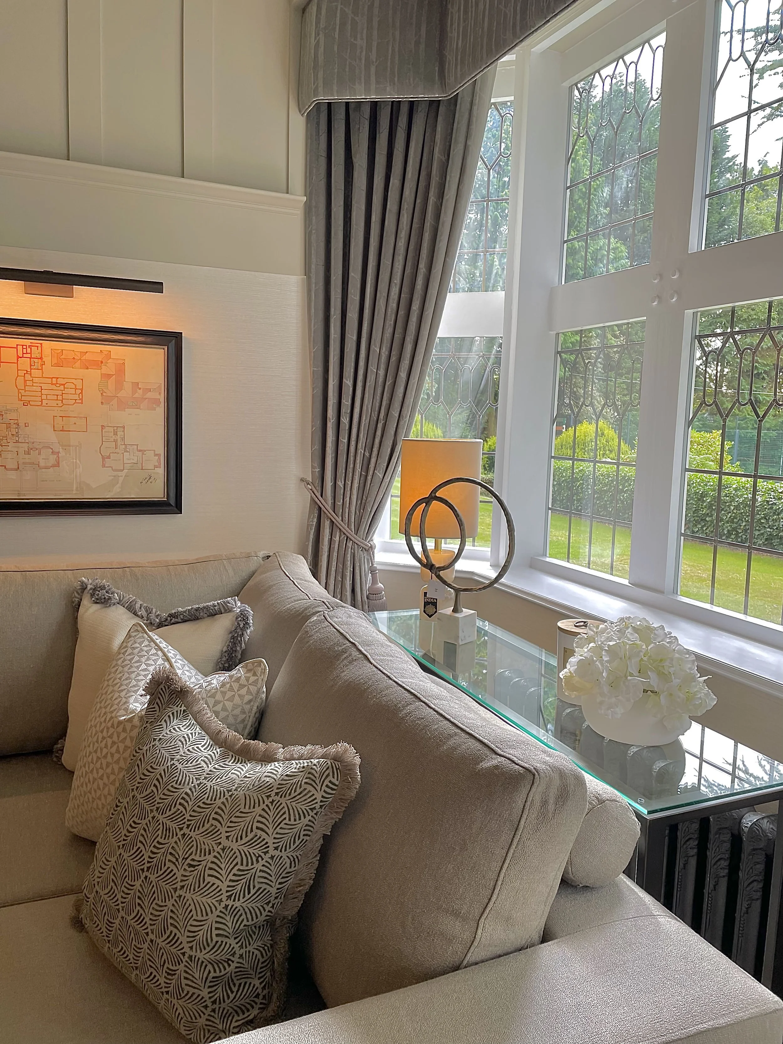 Living room corner featuring layered cushions, original leaded windows and tailored drapery in a Grade II listed family home.
