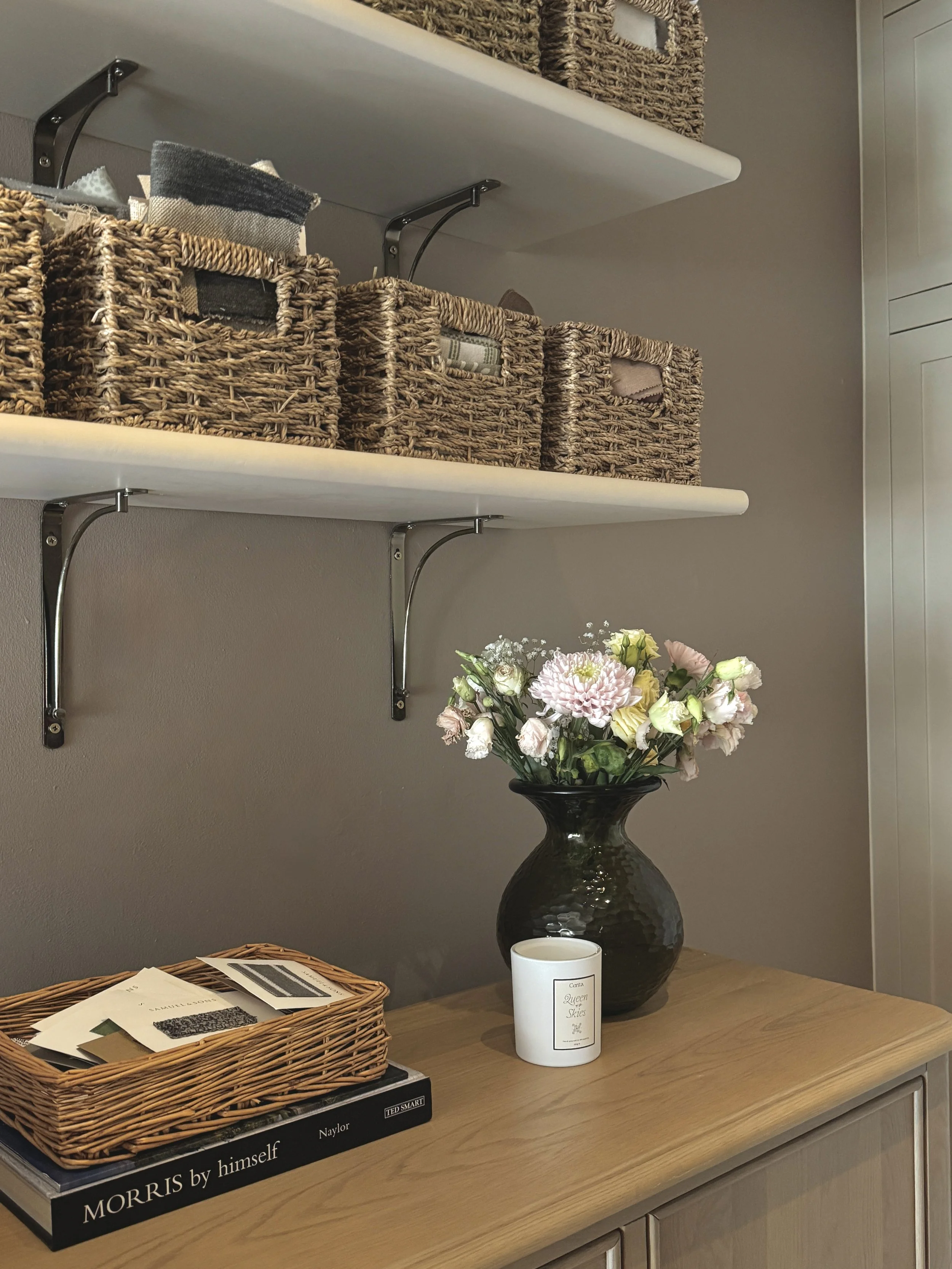 Interior design studio with fabric samples, woven storage baskets and material selections displayed on open shelves beside a wooden cabinet.