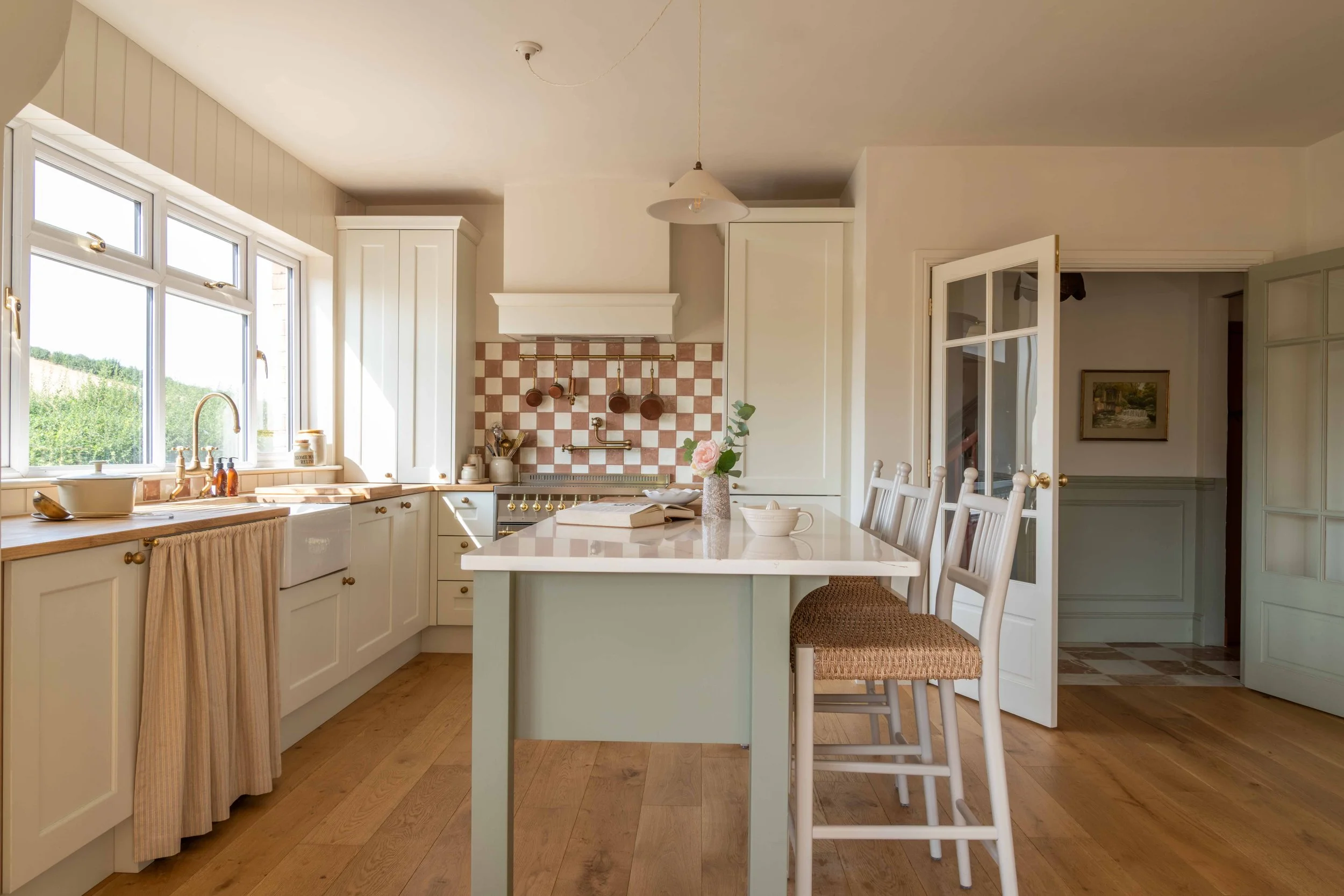 Traditional kitchen with a sage green island, cream Shaker cabinets, pink and white checkerboard tiles and brass fittings.