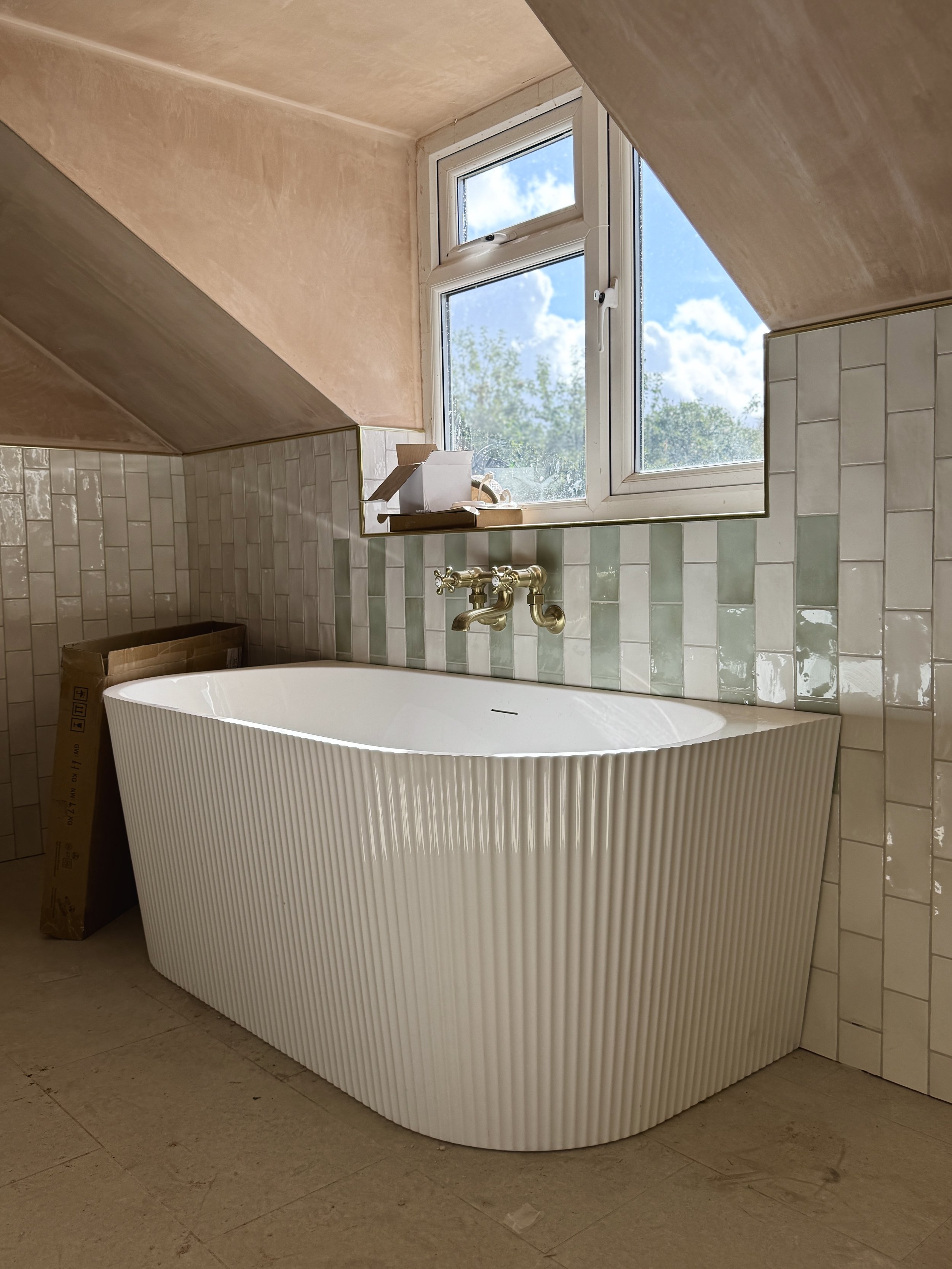 Fluted freestanding bath set against handcrafted glazed tiles and warm brass brassware in a refined family bathroom.
