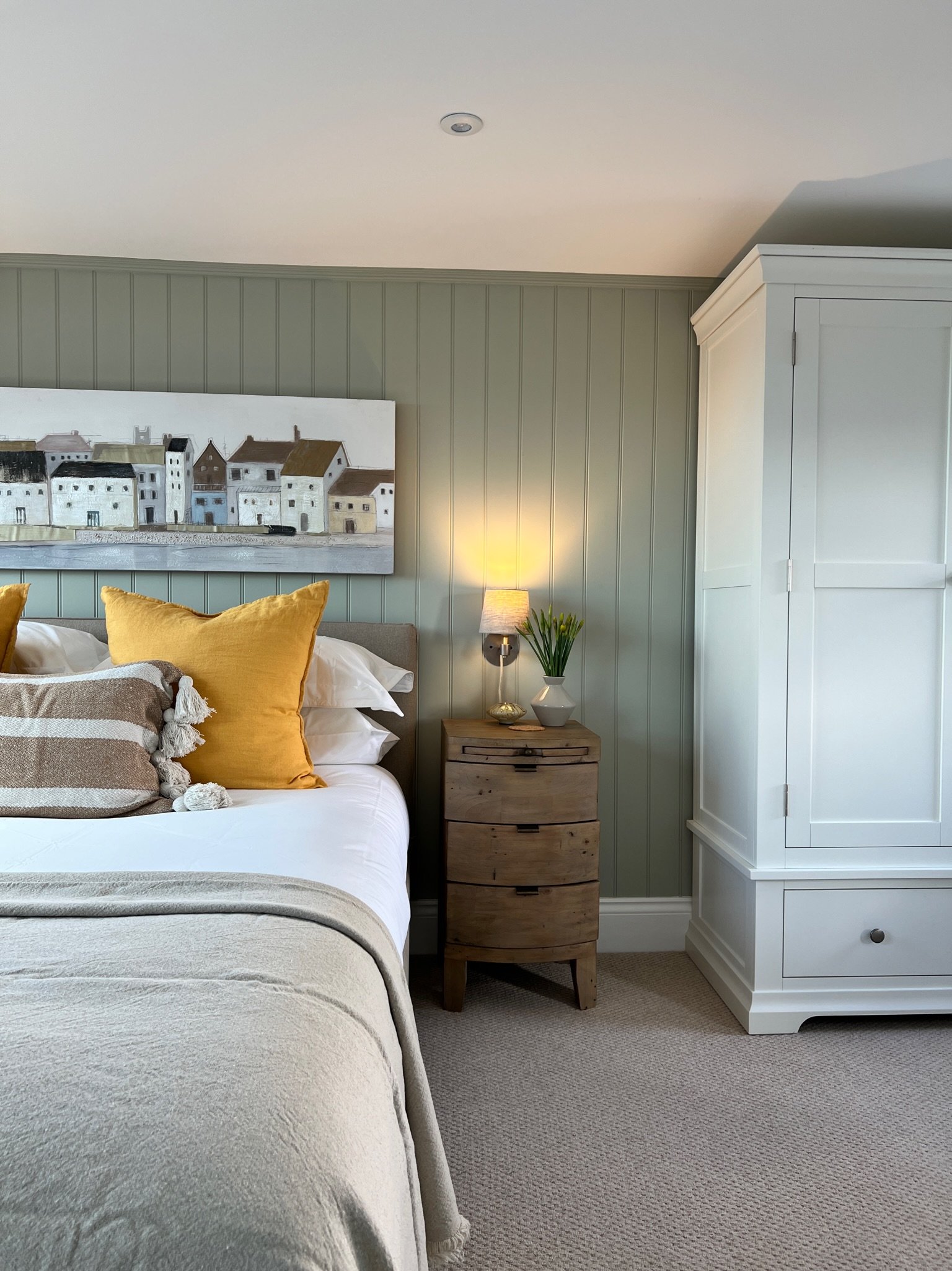 Bedroom with sage green tongue-and-groove panelling, natural wood furniture and layered soft furnishings at Project Brixham, Devon.