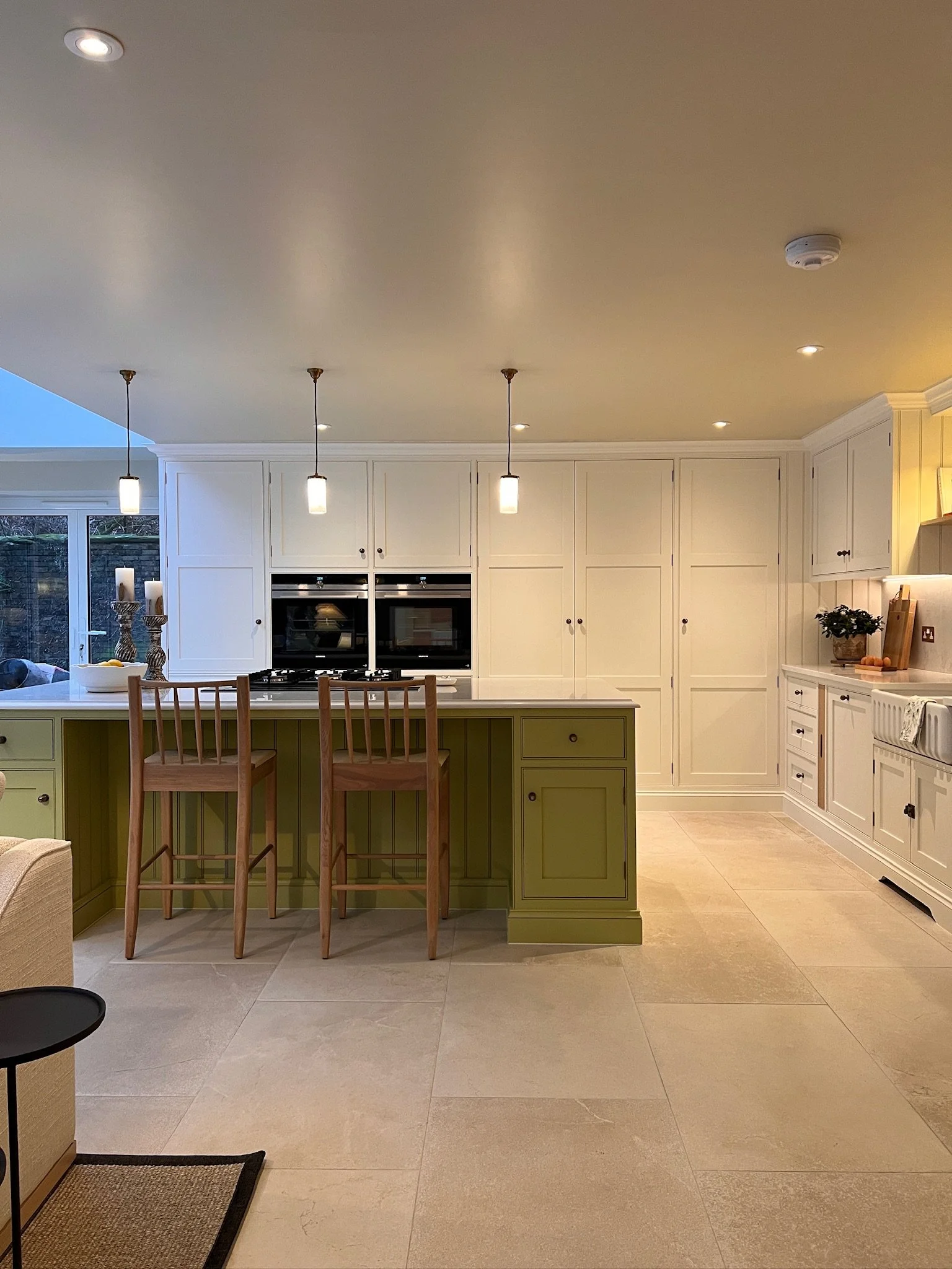 Custom shaker cabinetry with integrated farmhouse sink, brass hardware and layered lighting in a bespoke kitchen by Holly Oak House, Designed by Istigh Interiors, West Midlands.