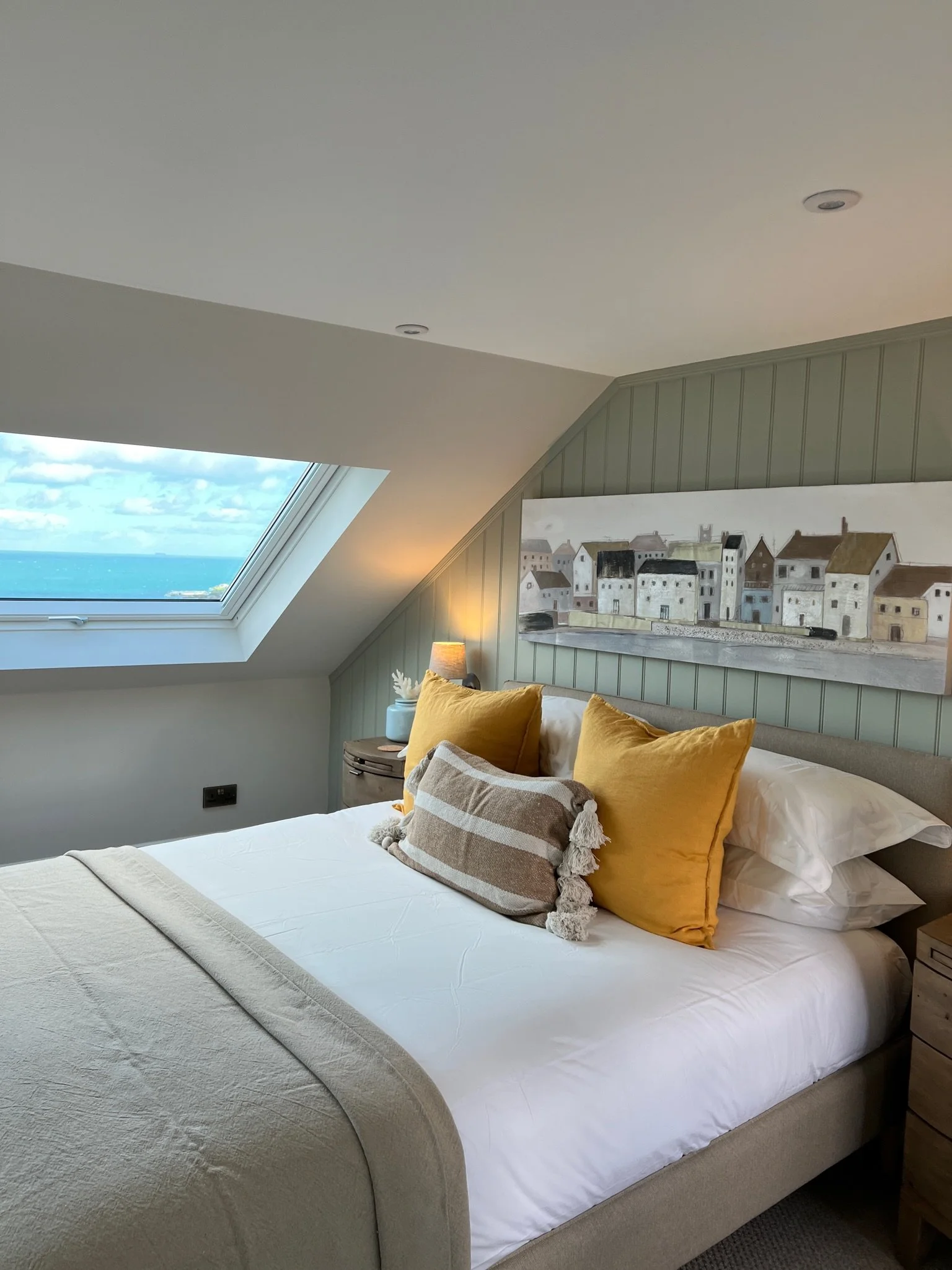 Bedroom at Project Brixham, Devon, featuring sage green wall panelling, warm neutral furnishings and a sea view through the rooflight.