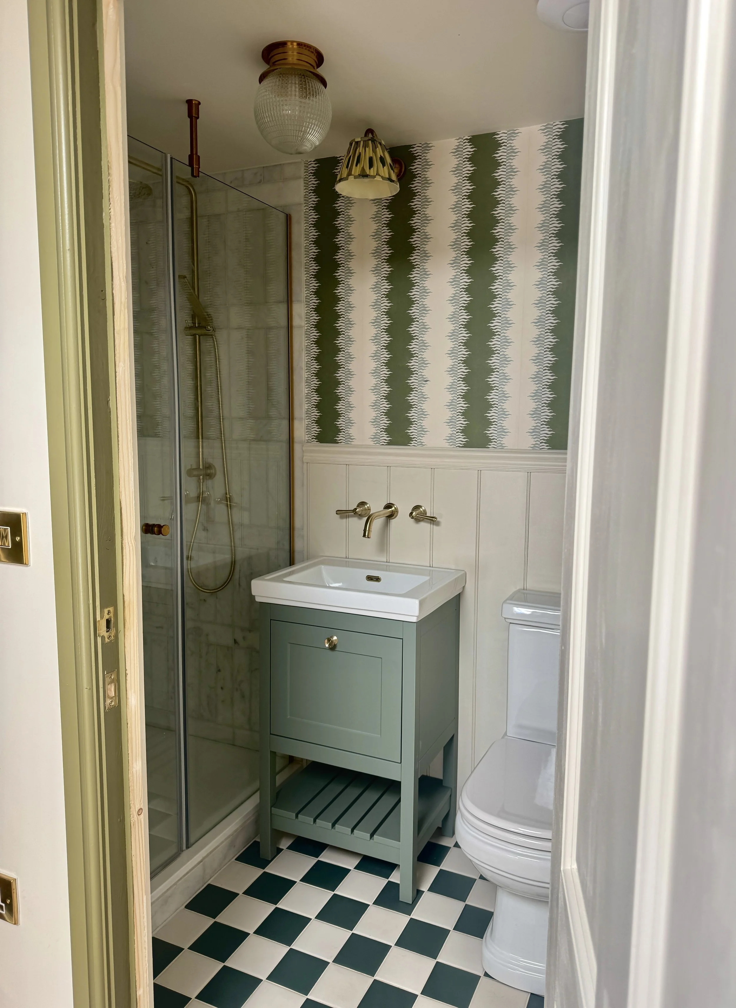 Green bathroom with striped wallpaper, brass fittings, checkerboard floor tiles and traditional vanity unit.