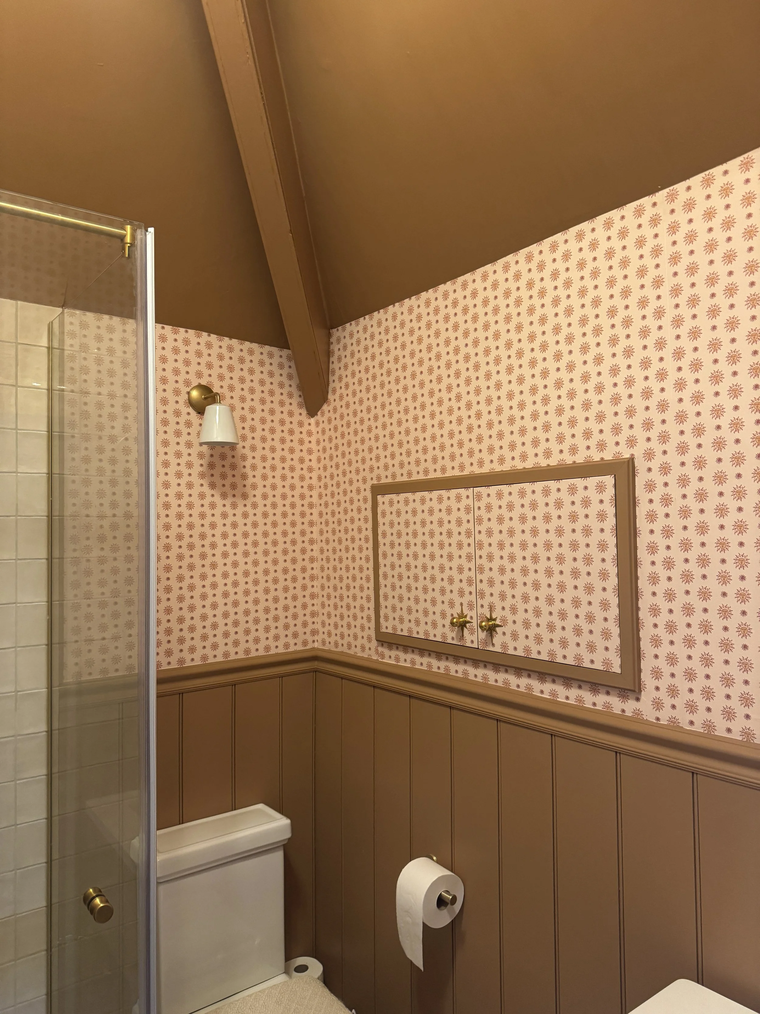 Traditional ensuite combining patterned wallpaper, painted panelling and brass wall lighting.