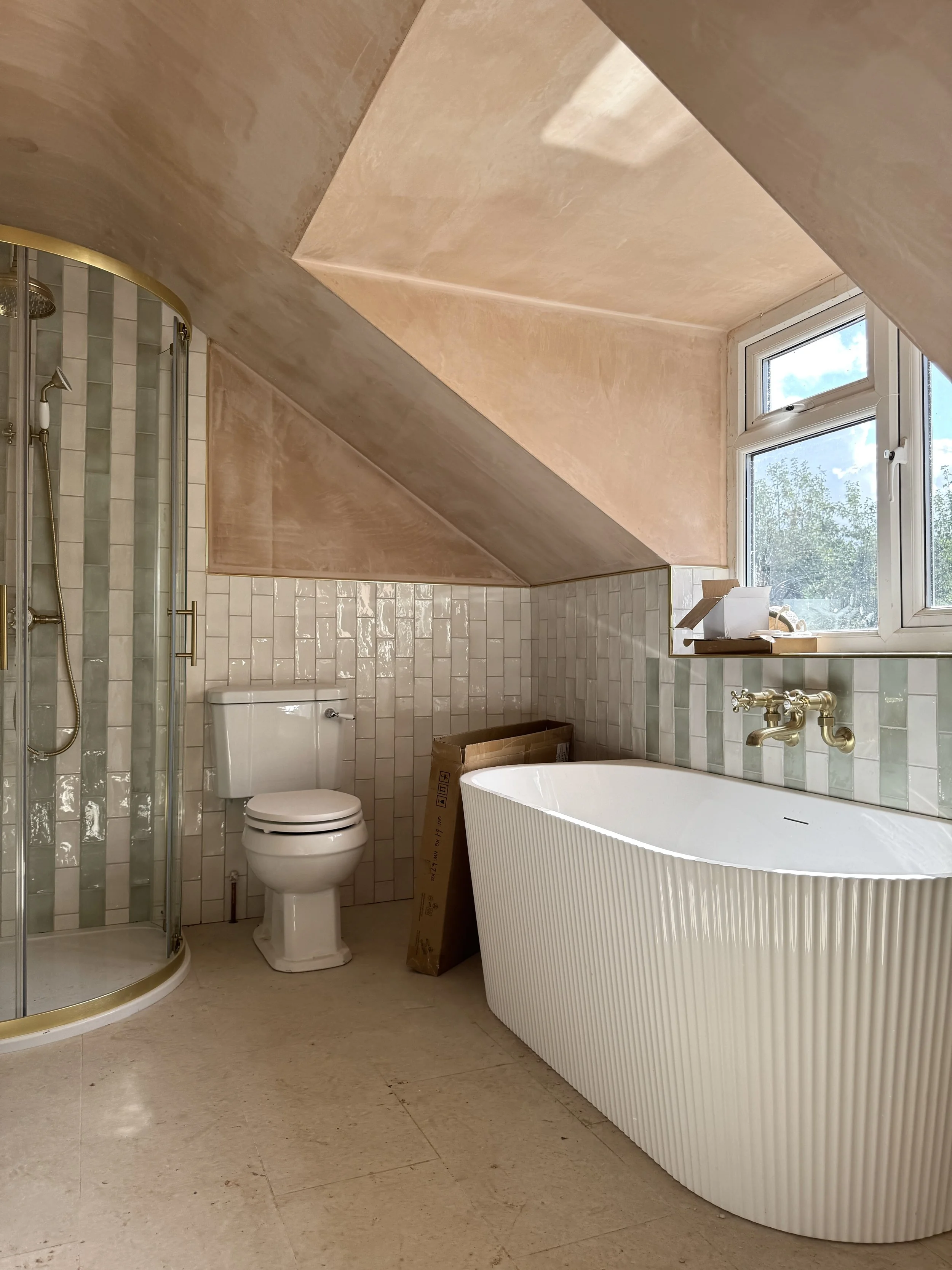Period-inspired bathroom featuring a fluted freestanding bath, glazed wall tiles, brass fittings and soft natural finishes.