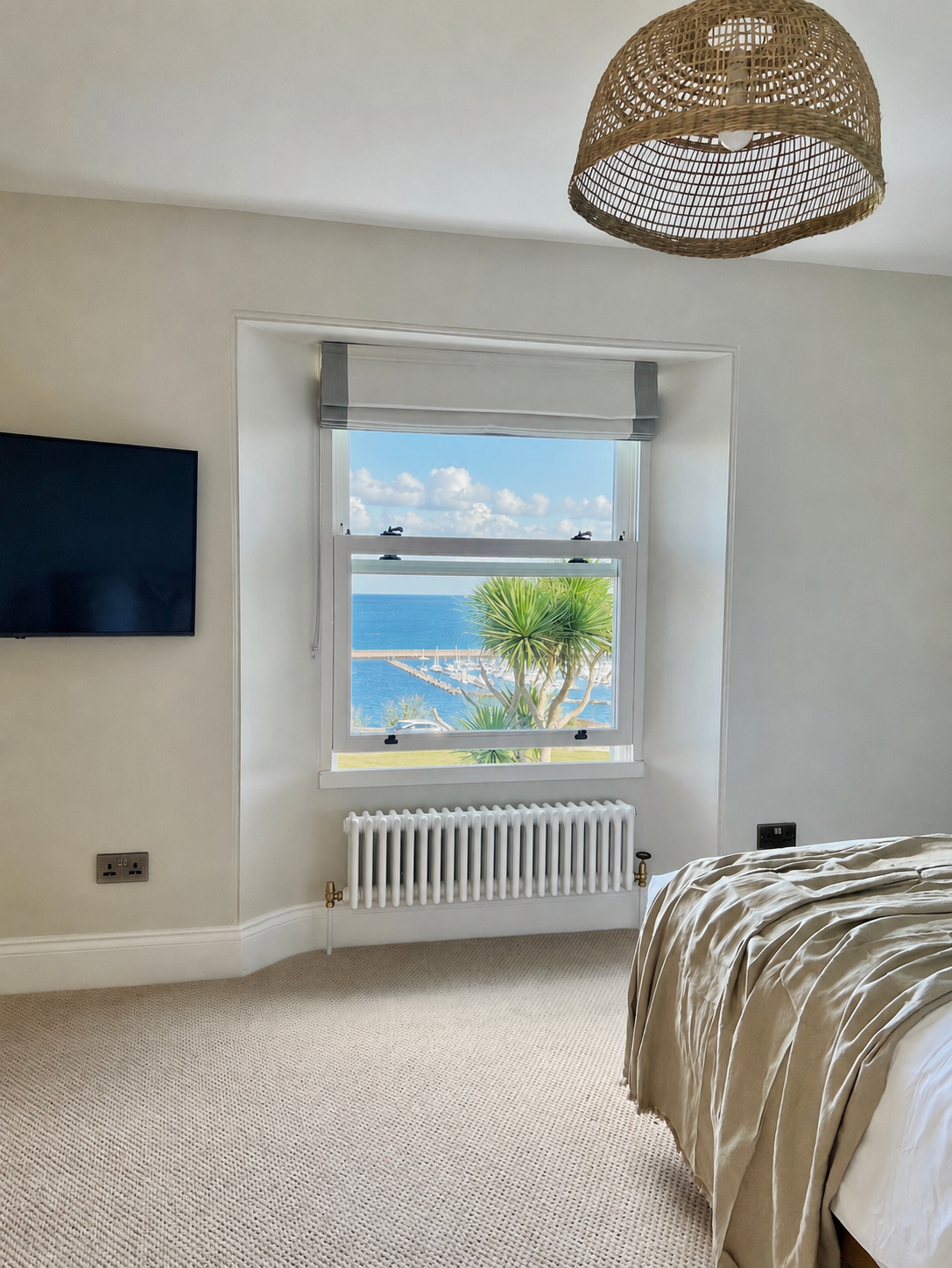 Guest bedroom overlooking Brixham Harbour with a woven pendant light, textured carpet and panoramic views.