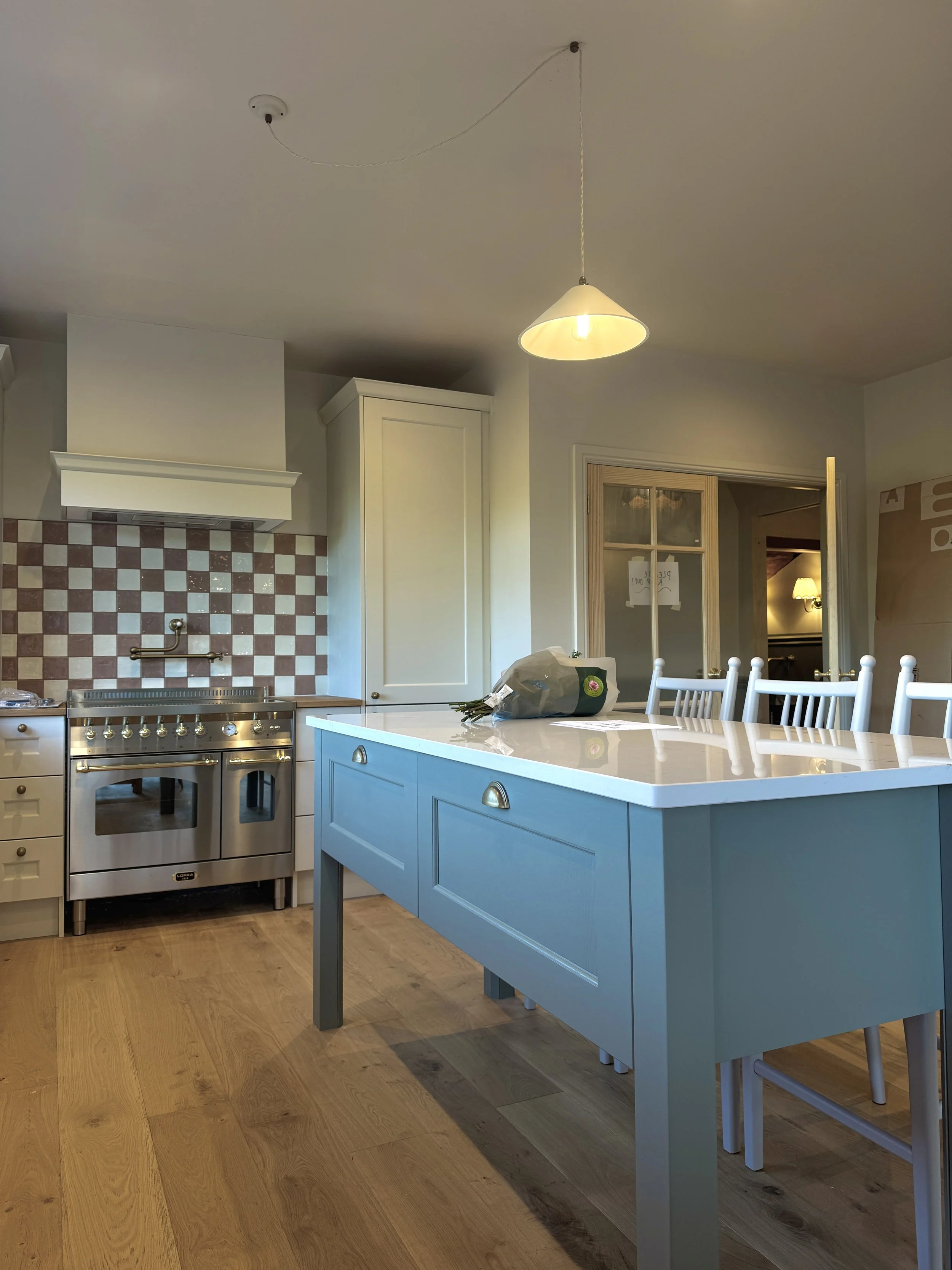 Painted shaker kitchen with blue island, pink checkerboard tiled splashback, quartz worktops and traditional brass detailing.