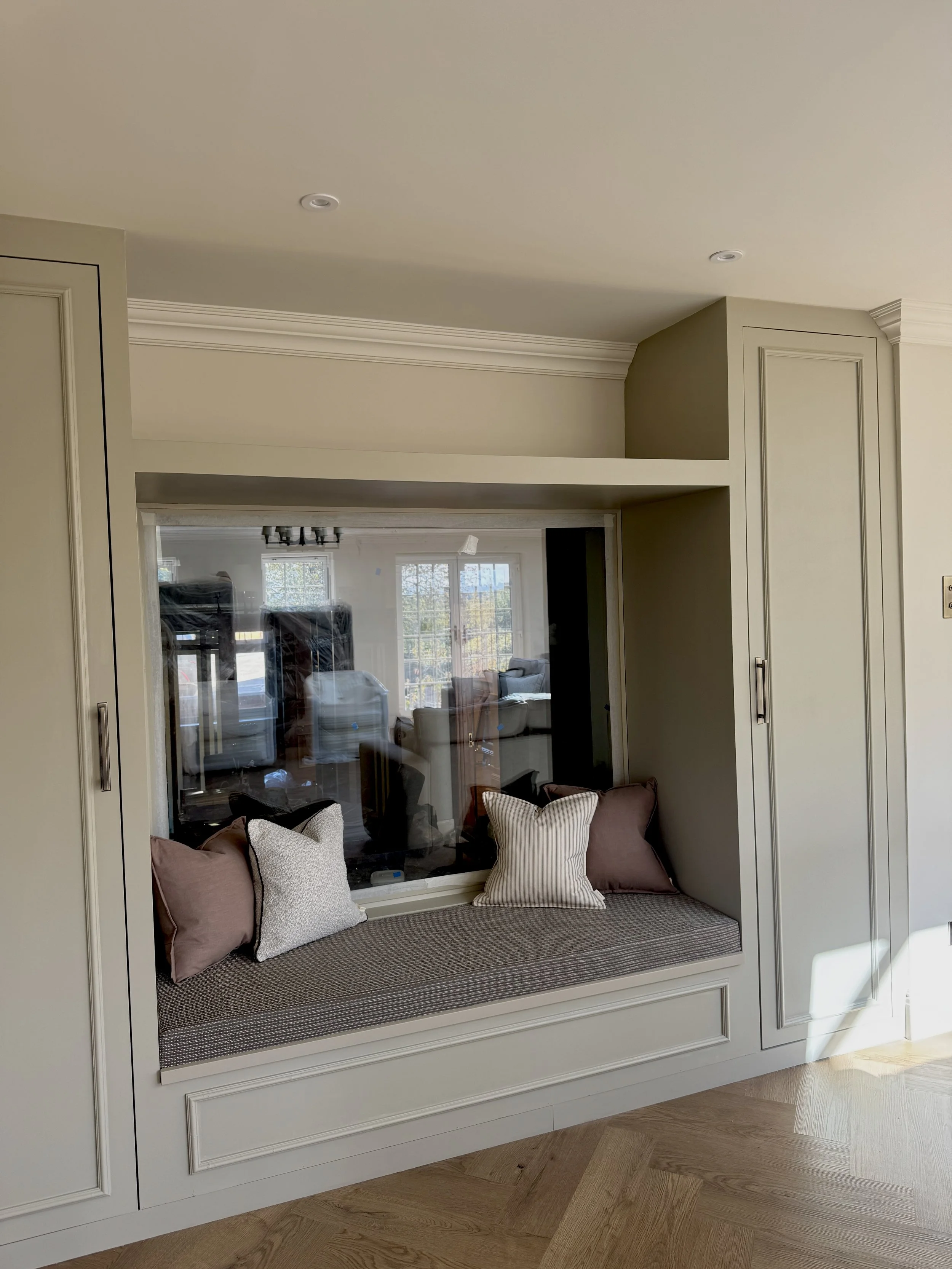 An upholstered window seat nestled within bespoke cabinetry provides a cosy reading nook and additional concealed storage, diving two rooms.