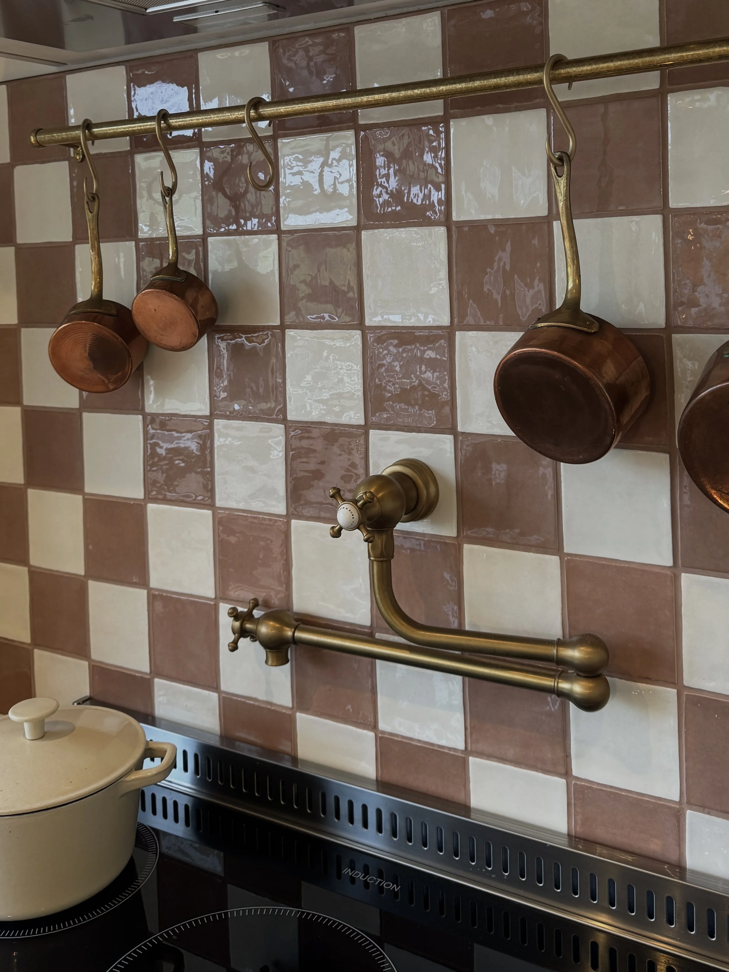 Handmade pink checkerboard tiled splashback with brass pot filler tap and traditional kitchen detailing.