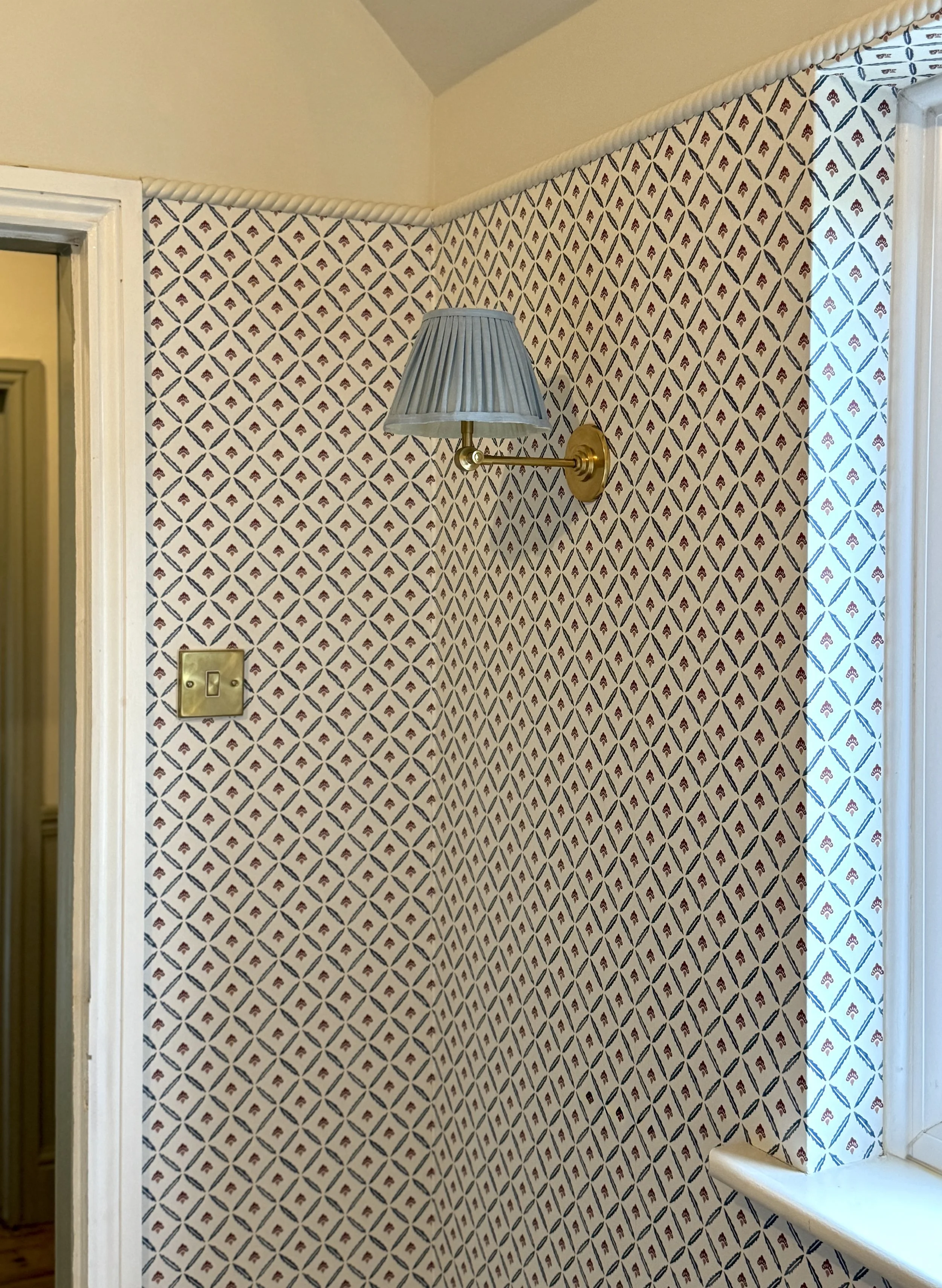Patterned wallpaper with a brass wall light, showcasing layered traditional interior design details.