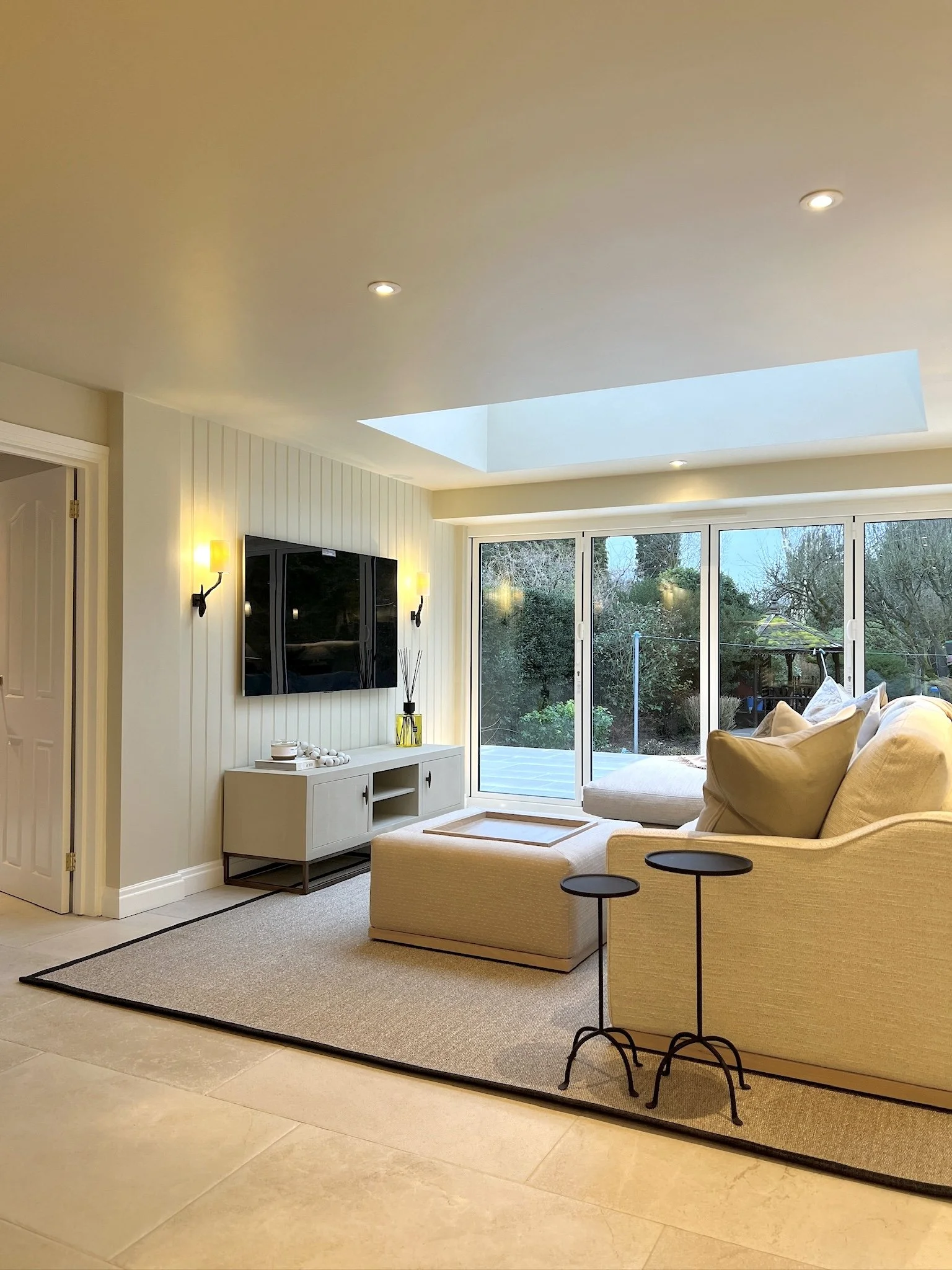 Light-filled open plan family living space with large bifold doors, skylight and layered neutral interiors in a West Midlands home by Istigh Interiors.