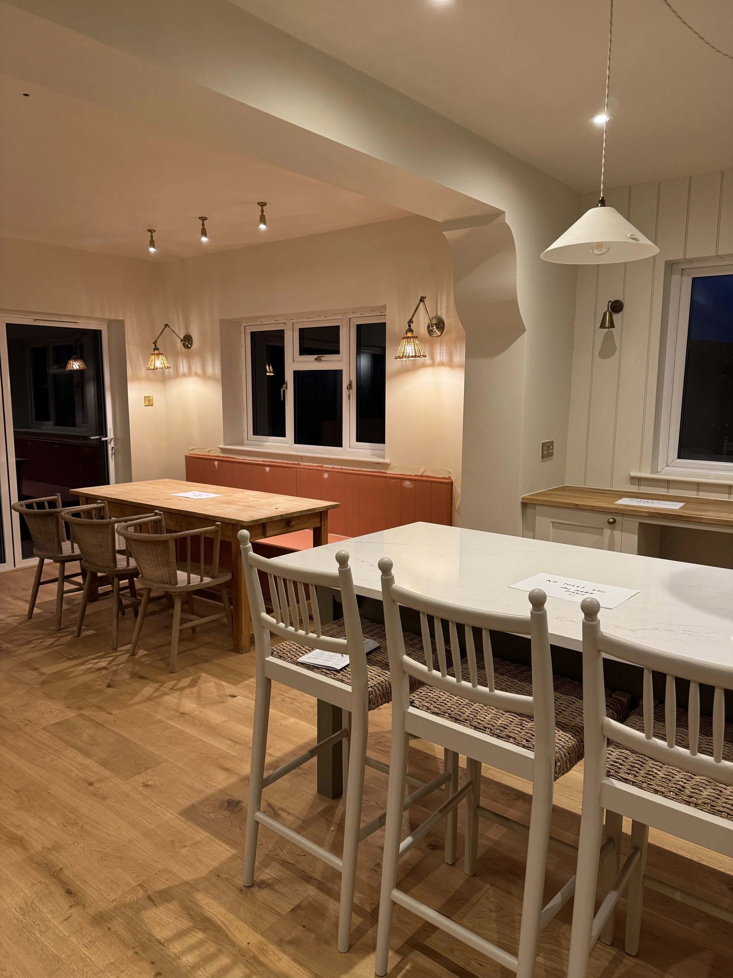 Bespoke family kitchen with handmade banquette seating, oak flooring, detailed opening and brass wall lighting.