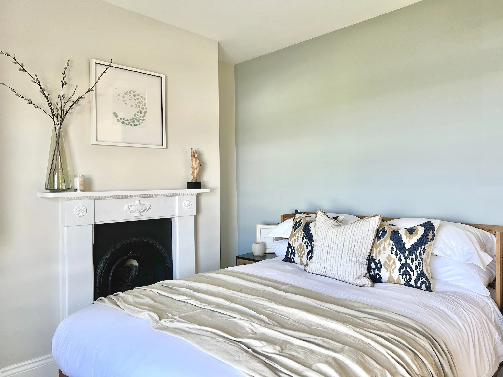 Guest bedroom with soft blue feature wall, restored fireplace, natural oak furniture and layered neutral textiles in a thoughtfully designed Brixham home.