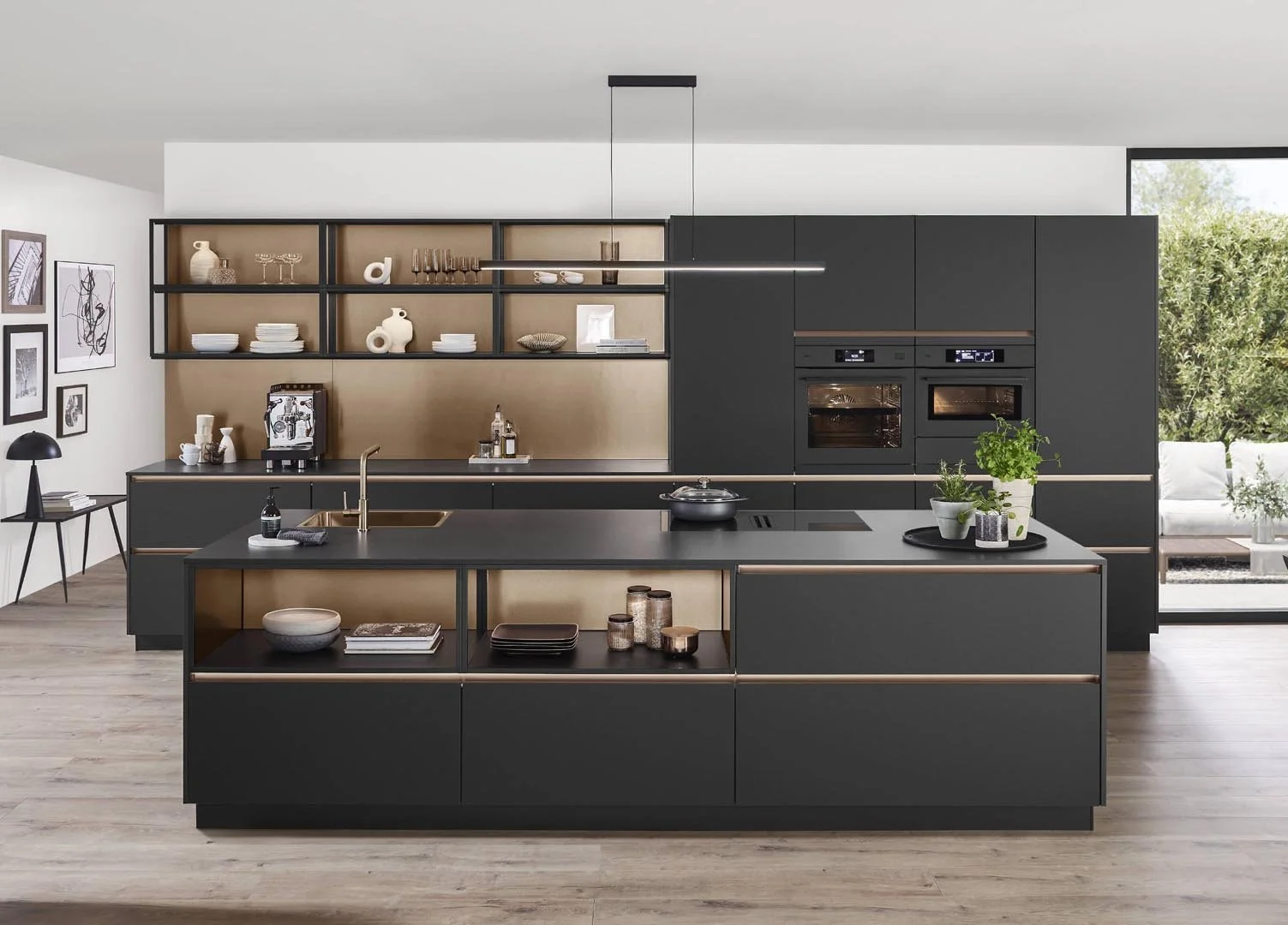 Modern kitchen with black cabinets and open shelving, containing white dishes, glassware, decorative items, and a coffee machine. Contains a central island with a black countertop, plants, and a stove, with a sliding glass door showing outdoor seatin
