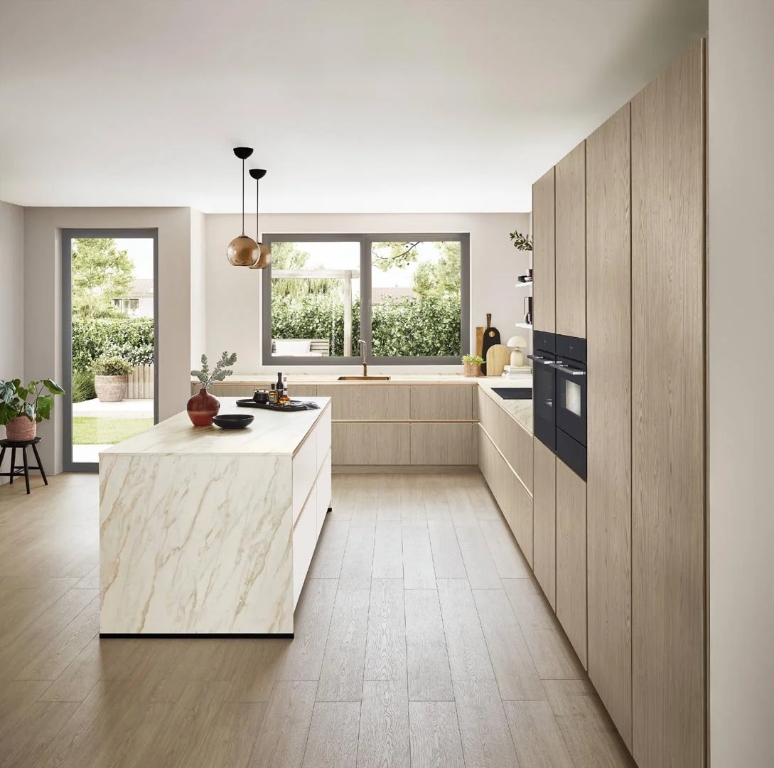 Modern kitchen with light wood cabinetry, a marble island, large windows, and outdoor view.