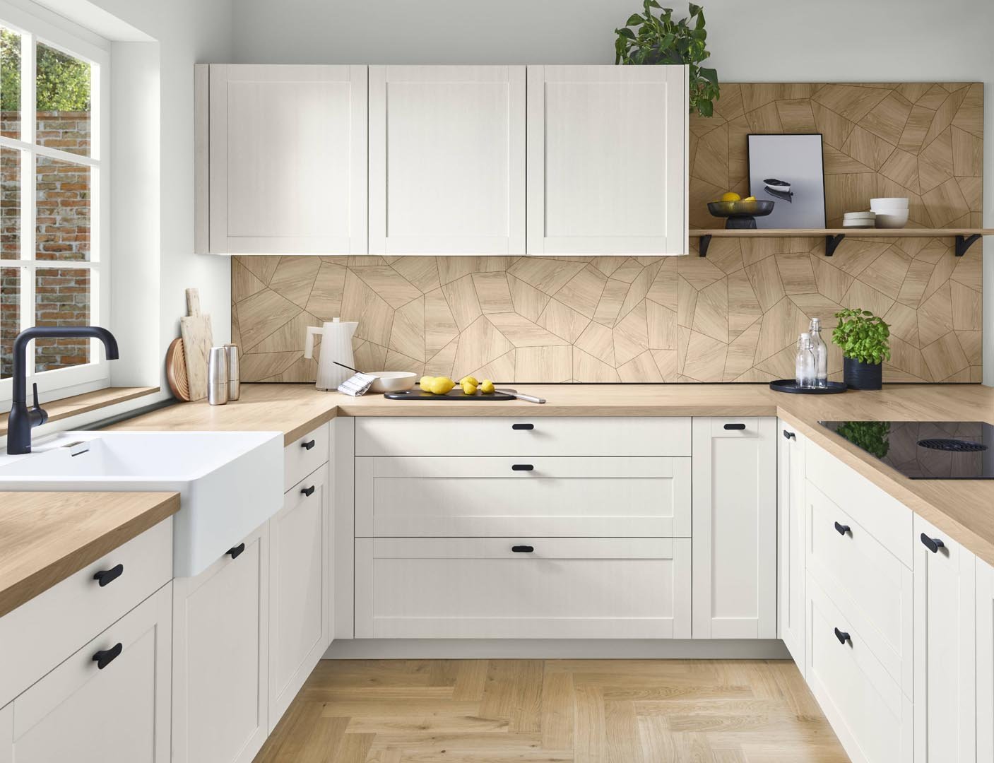 Modern kitchen with white cabinets, wooden countertops, geometric wood backsplash, black hardware, and a window with greenery outside.