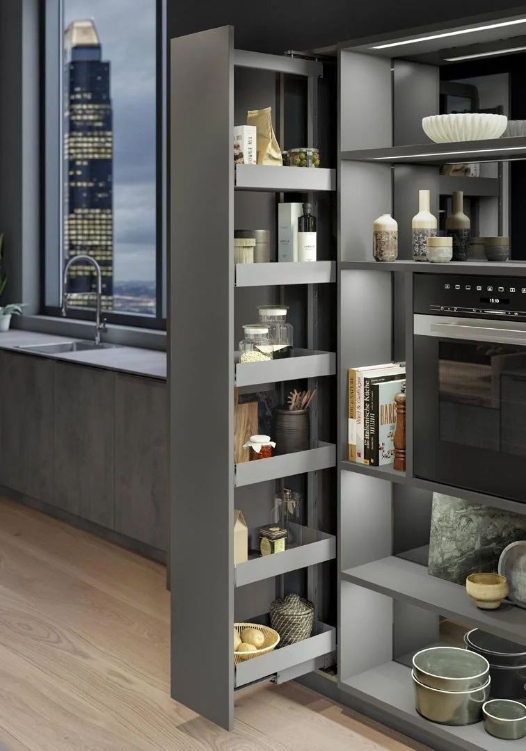 Close-up of gray kitchen shelving with various jars and books, next to a window overlooking a cityscape with tall buildings.