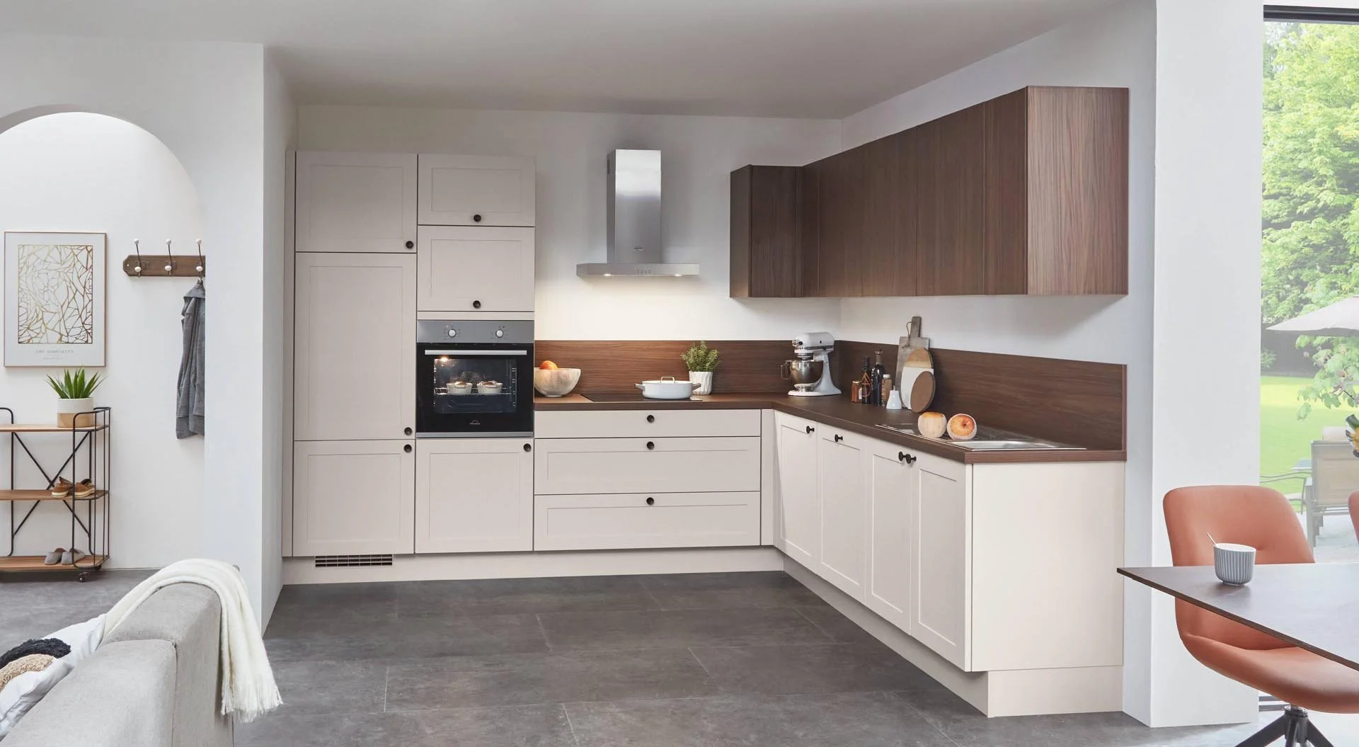 Modern kitchen with white and wooden cabinetry, stainless steel range hood, black countertops, and a view of an outdoor patio with green trees and an umbrella.