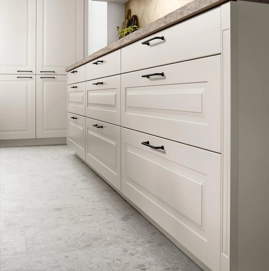 White kitchen cabinets with black handles and a beige countertop, with a plant on top.