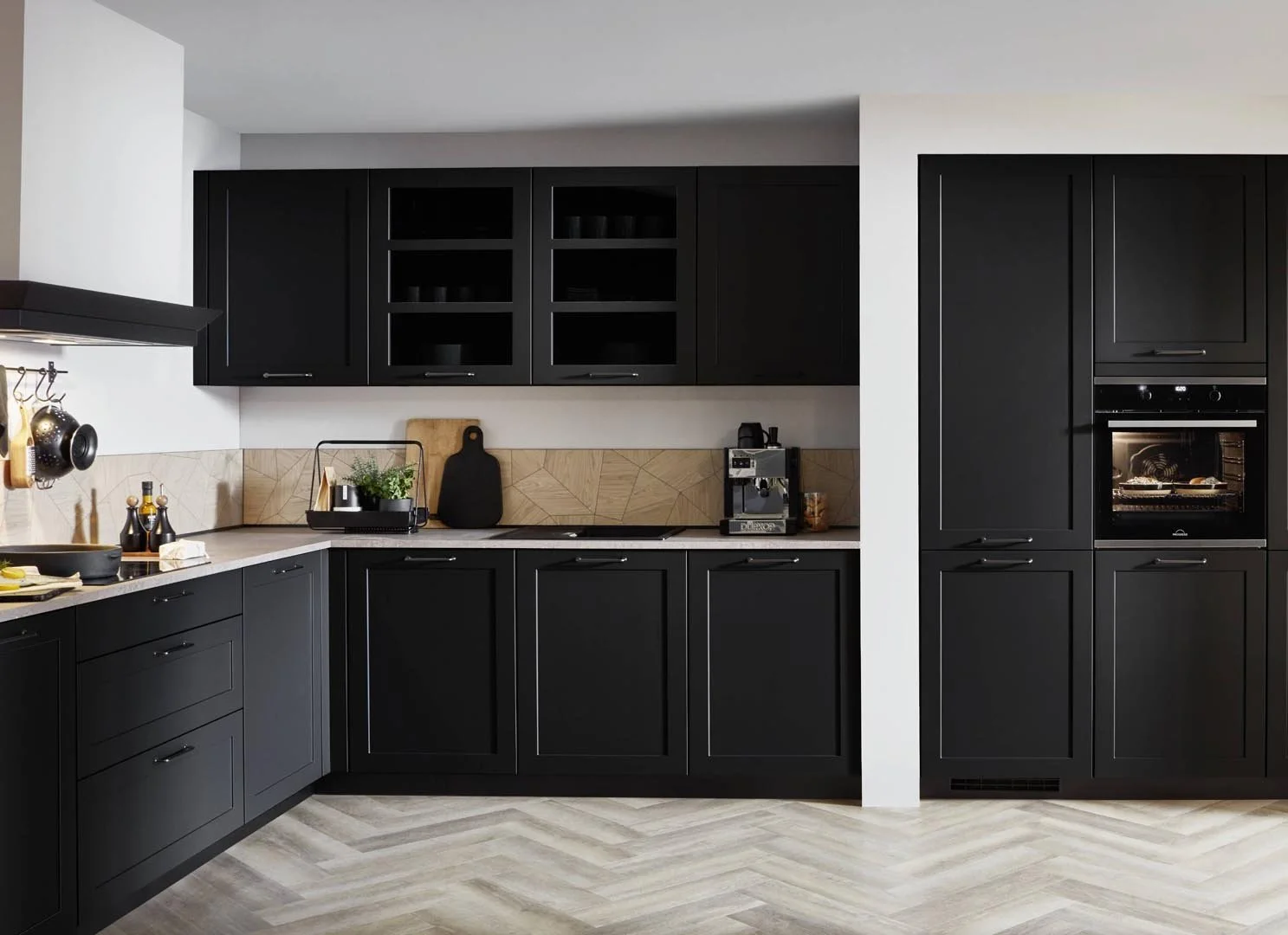 Modern kitchen with black cabinets, beige countertops, and patterned backsplash, featuring kitchen appliances and utensils.