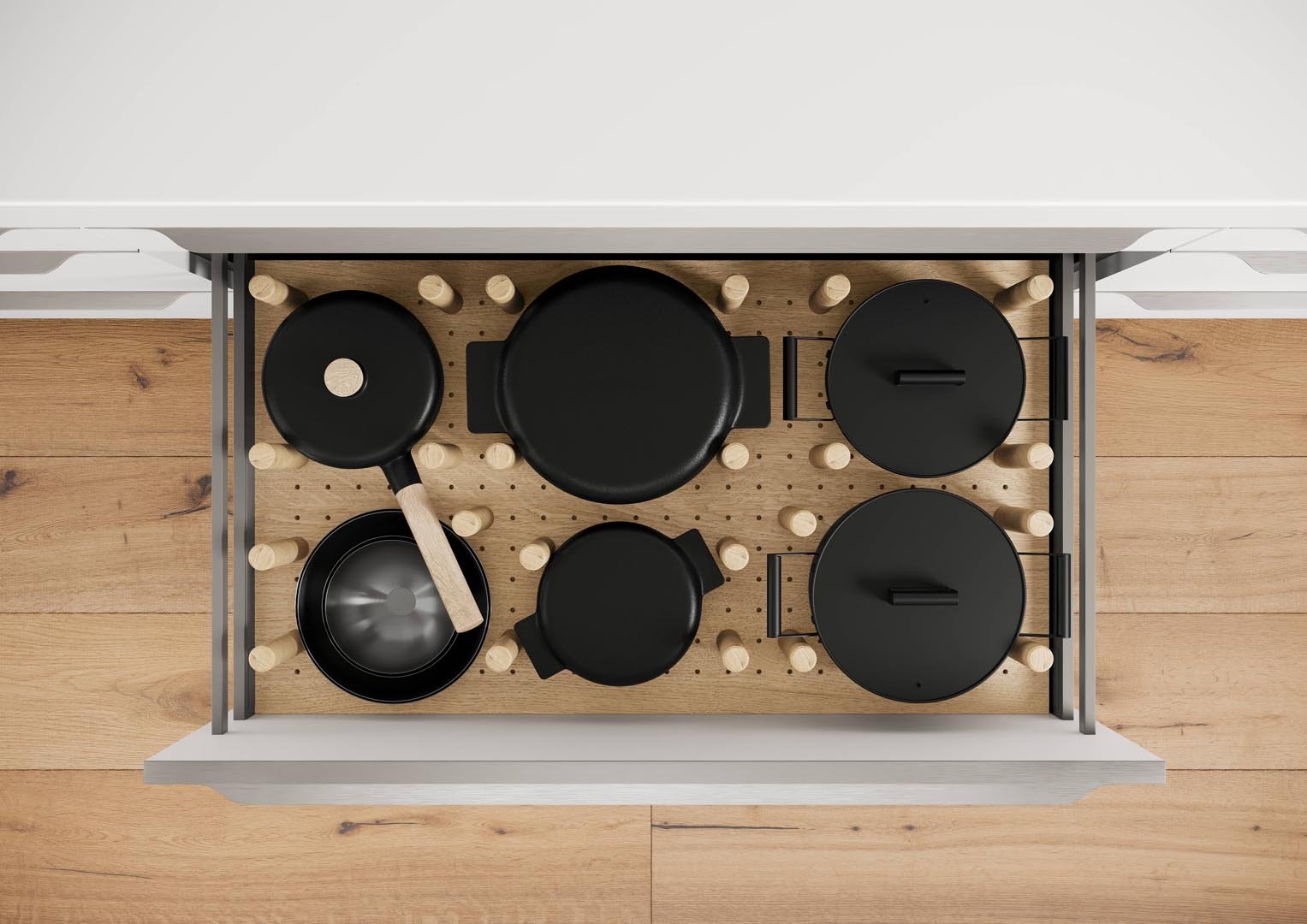 Overhead view of a wooden kitchen drawer filled with black cookware, including a small pan, a wok, two lids, and a skillet.