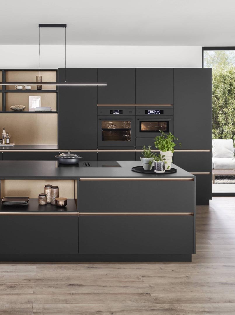 Modern kitchen with black cabinets, built-in oven, and a kitchen island with potted plants.