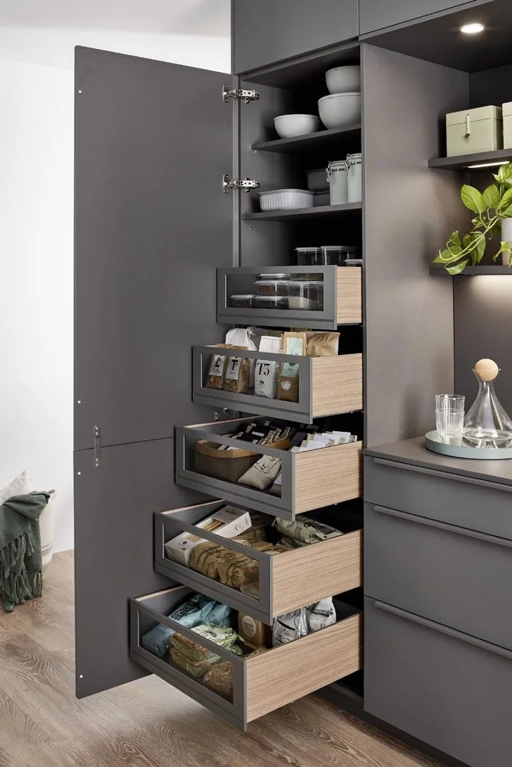 A modern kitchen cabinet with open drawers containing packaged food items, and shelves with dishware and kitchen supplies.