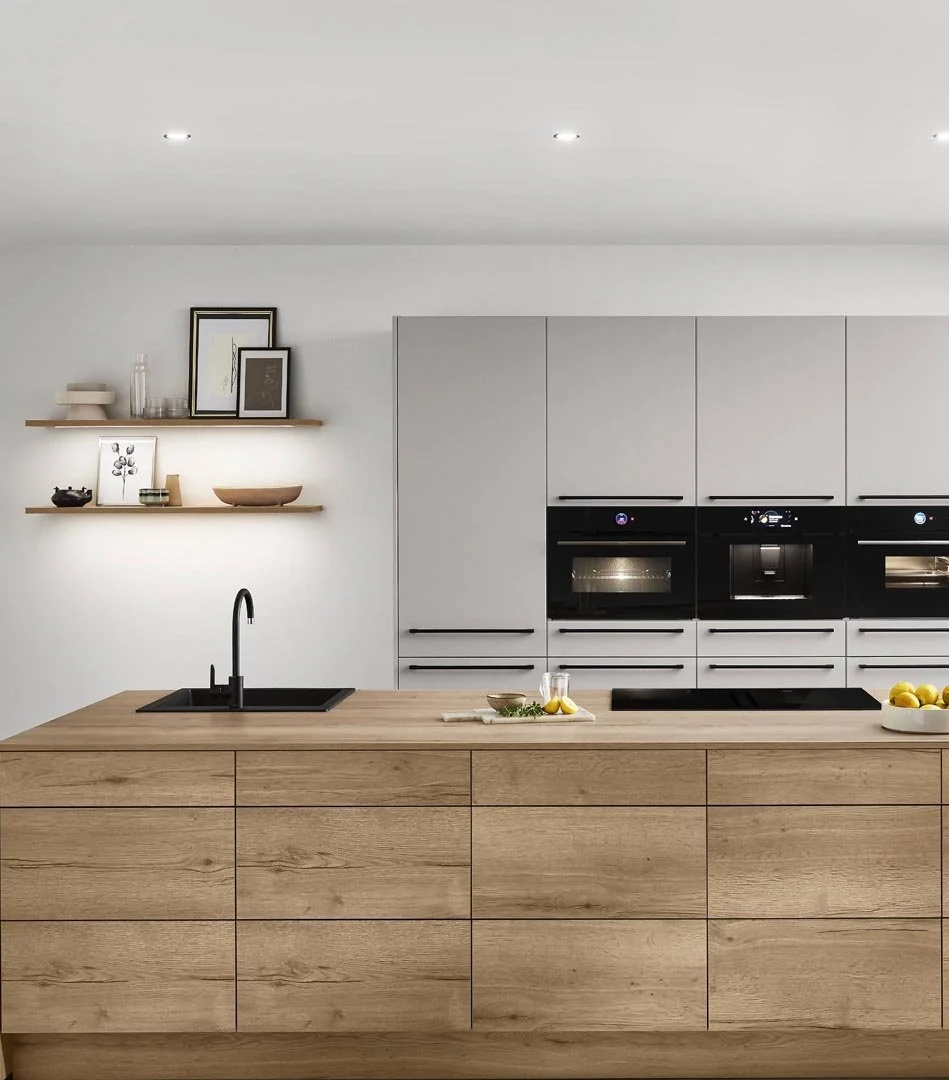 Modern kitchen with light gray cabinets, black built-in ovens, a wooden island with a sink, black faucet, and a bowl of lemons.
