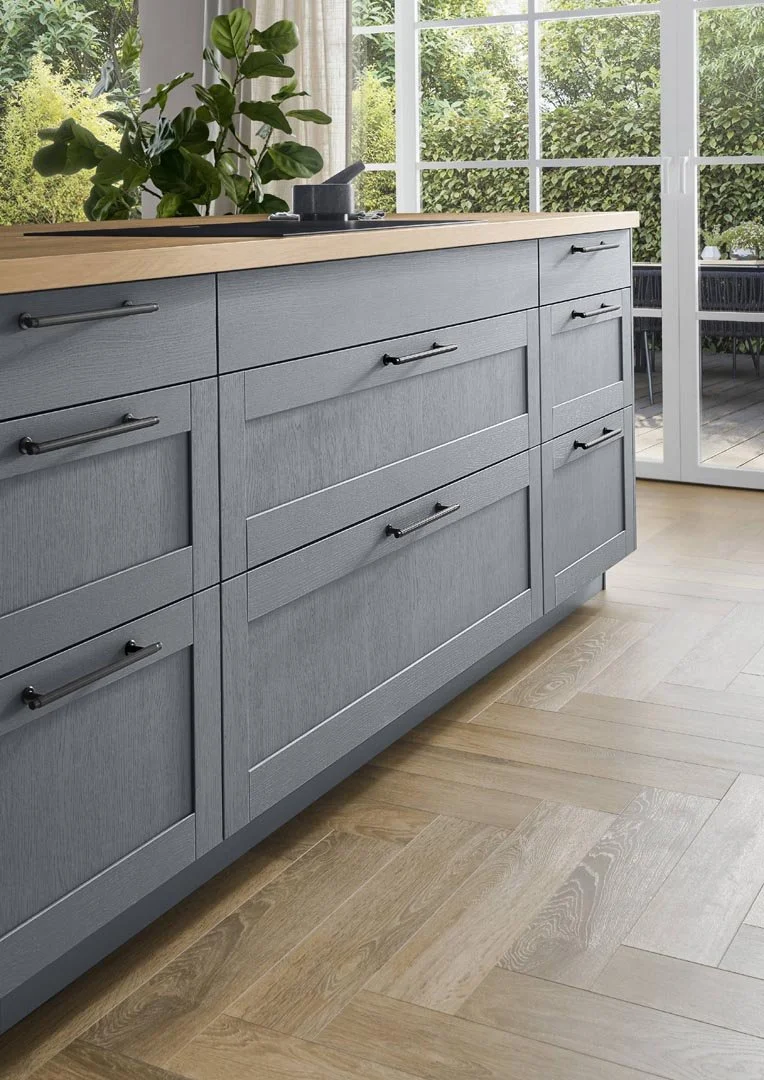 A kitchen countertop with gray cabinets and black handles, a potted plant, and a view of a backyard patio through large glass doors.
