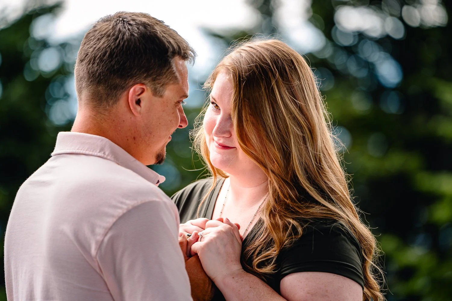 A romantic moment between a man and woman outdoors, holding hands, looking into each other's eyes with a blurred green background.