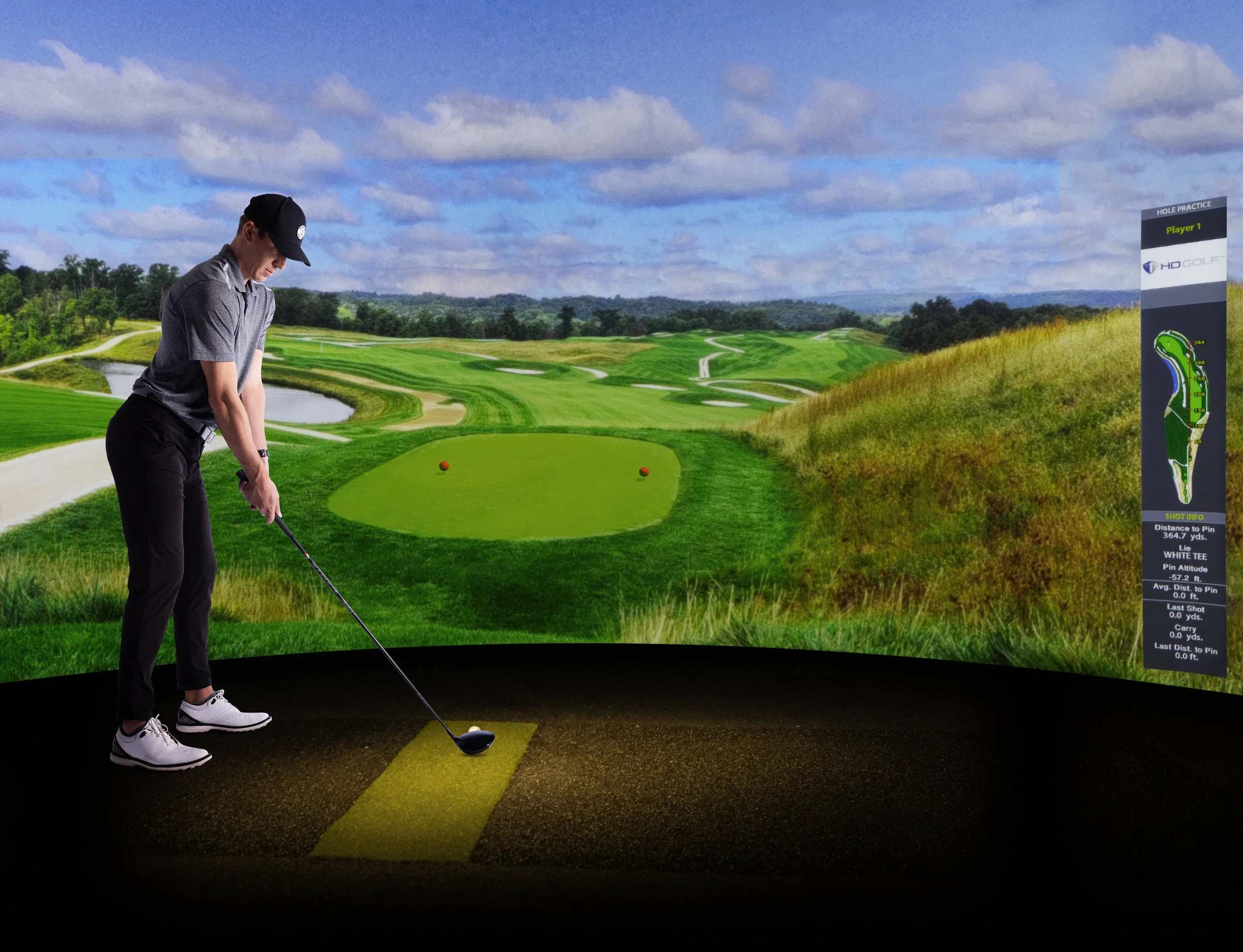 Man practicing golf indoors with a virtual golf simulator showing a scenic golf course on the screen.