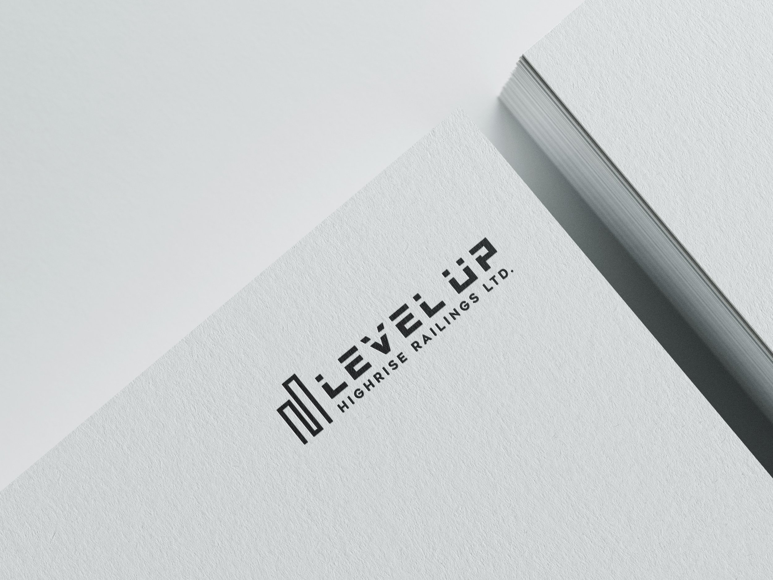 Close-up of a white sheet of paper with a black logo and text reading 'Highrise Railings Ltd.' on a textured surface, with a stack of blank paper nearby.
