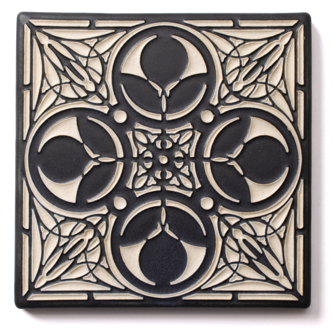 A decorative black and beige silicone trivet with a geometric design featuring moons, circles, and spiderweb patterns.
