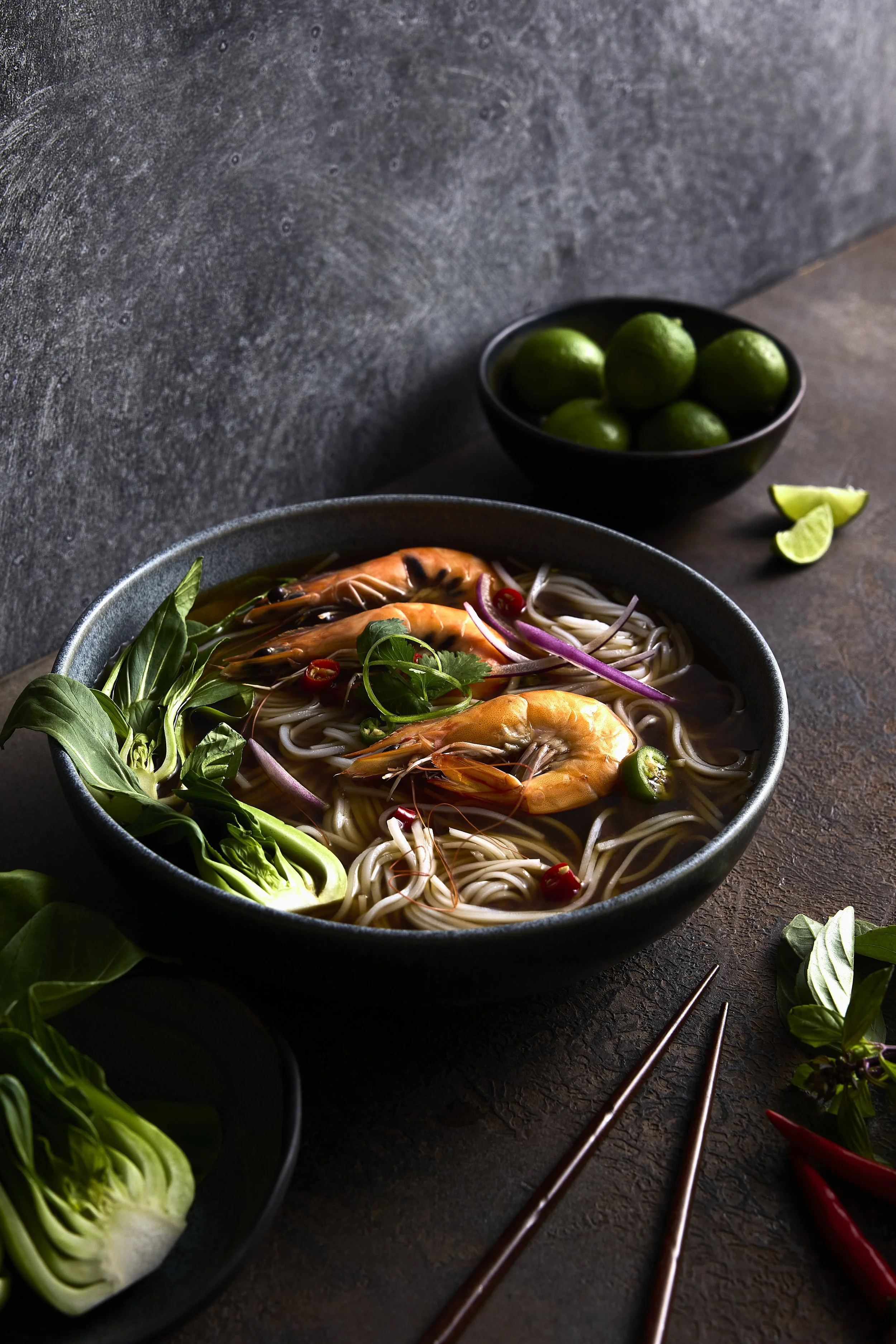 bowl of pho with limes and veggies