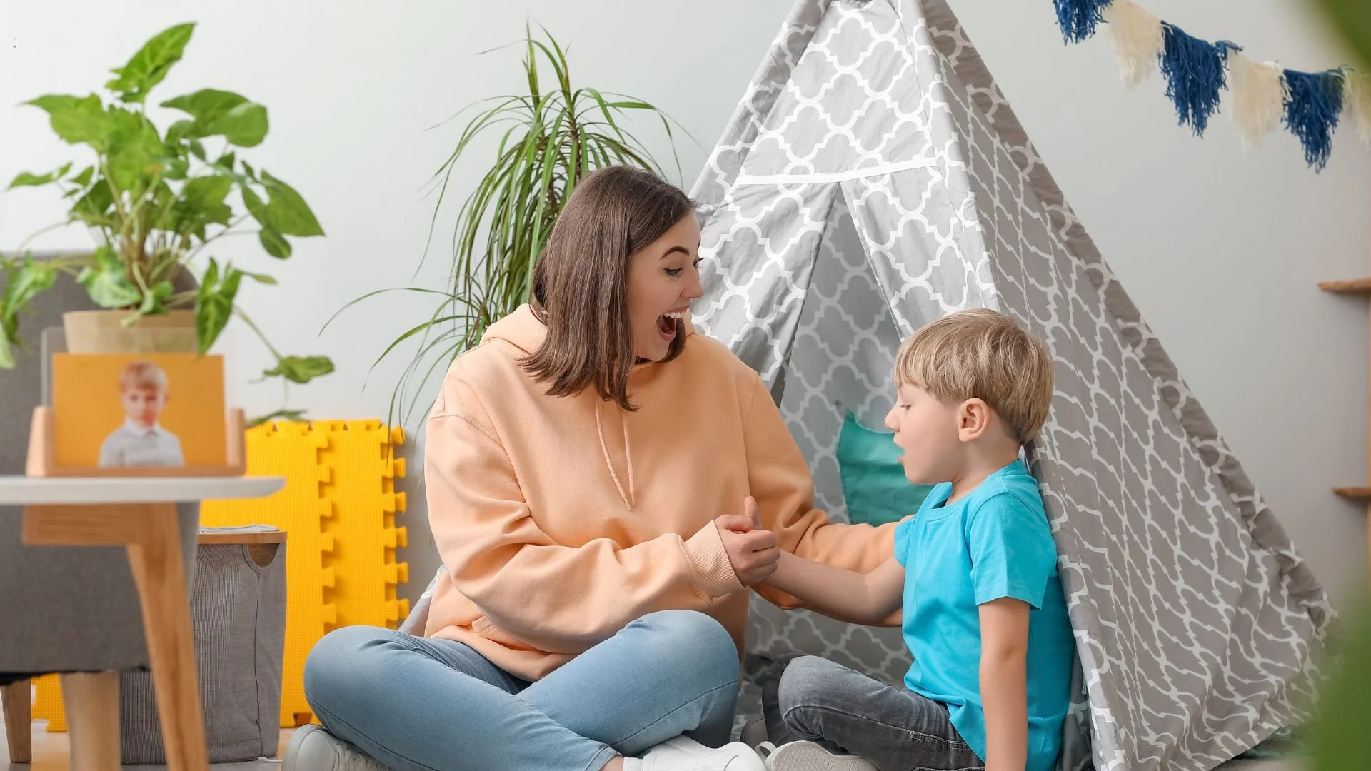 Professional nanny playing on the floor with two toddlers in a bright, clean playroom.
