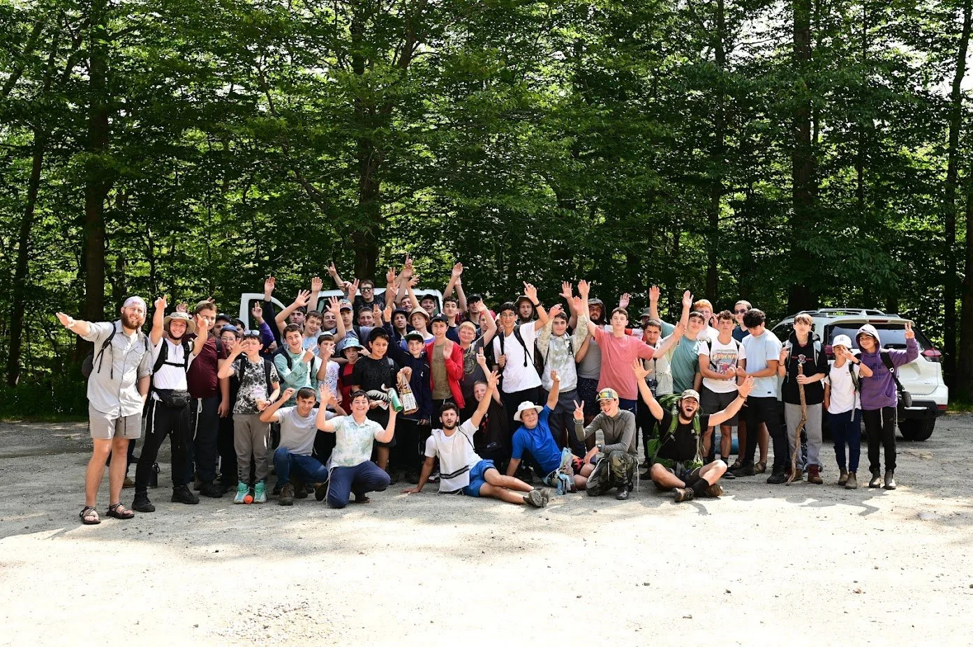 Group of people posing outdoors in a wooded area with raised hands and smiling.