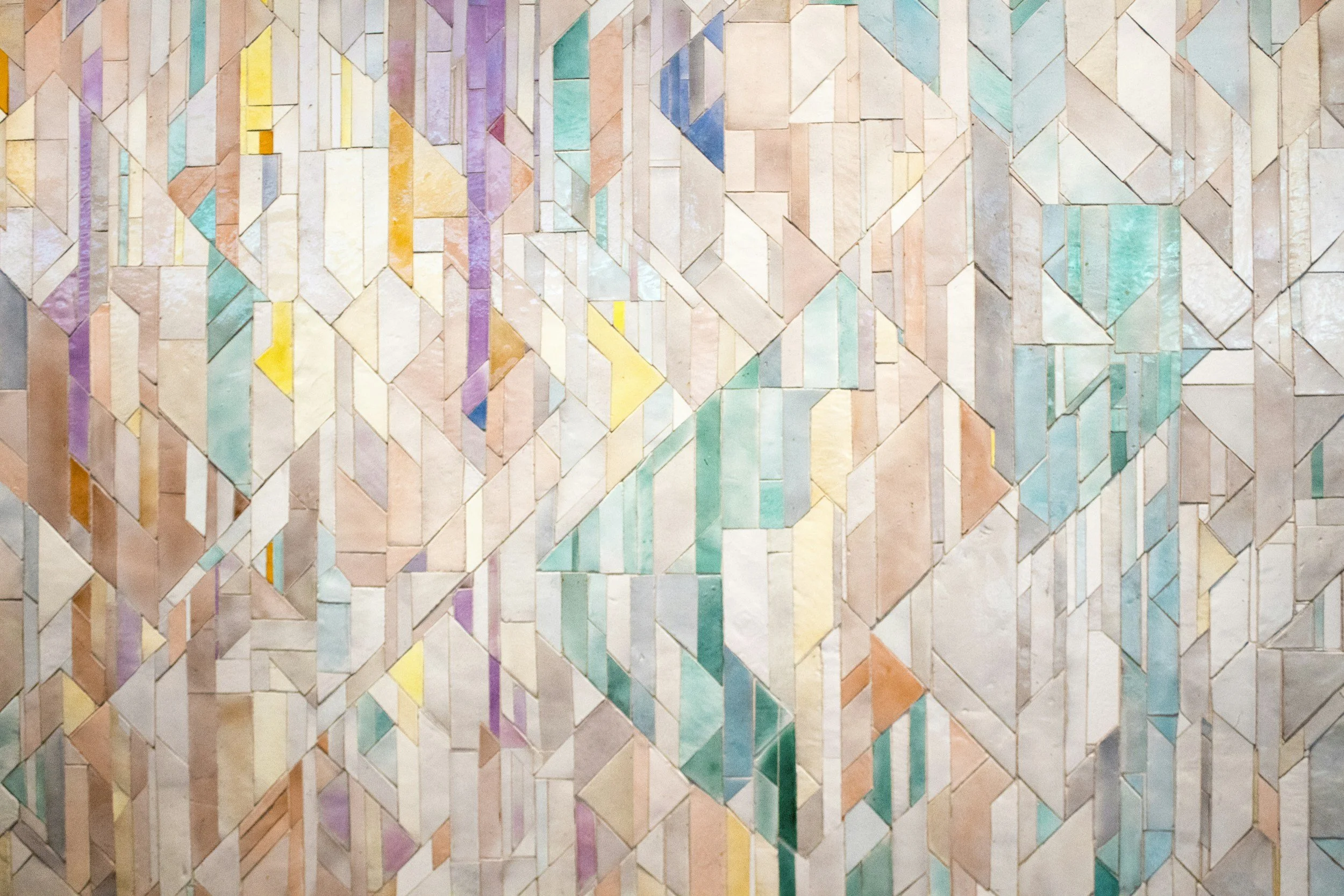 Colorful geometric mosaic wall with various shapes and pastel shades of pink, purple, blue, yellow, and green.