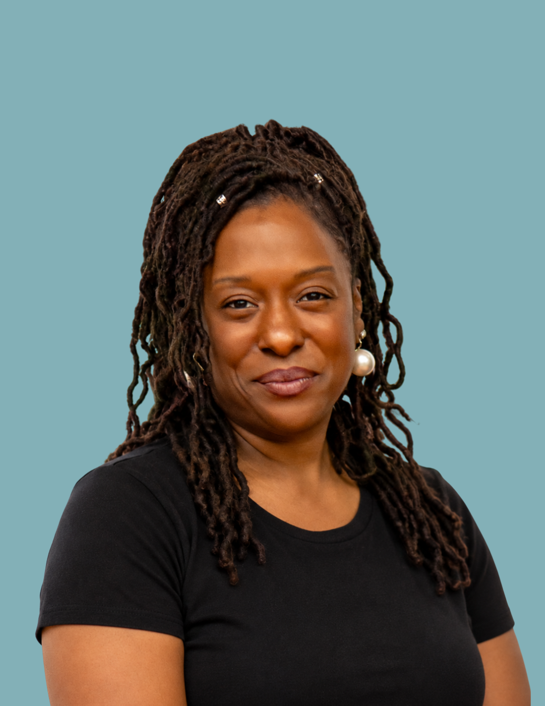 Natalie Williams, Care Coordinator at UBH, with long braided hair with red tips, wearing a black and white zebra print blouse and pearl earrings, smiling against a teal background.