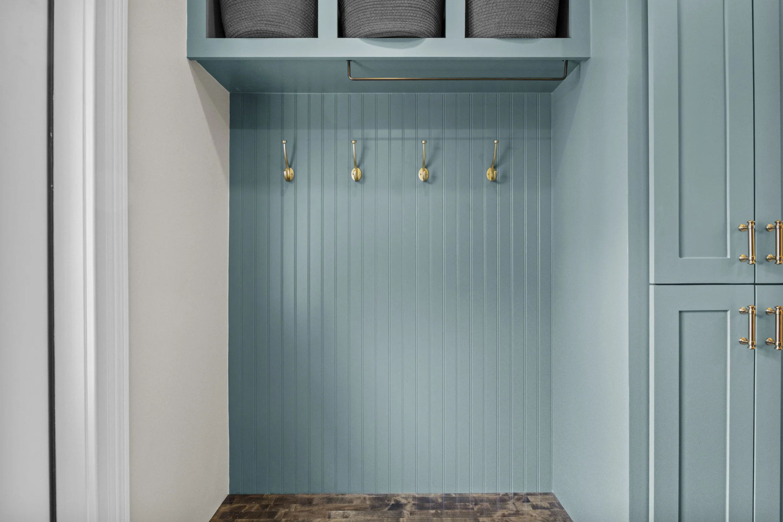 Close-up of a teal-colored wooden wall with four brass hooks, a brass handle, and a decorative wooden section at the top.