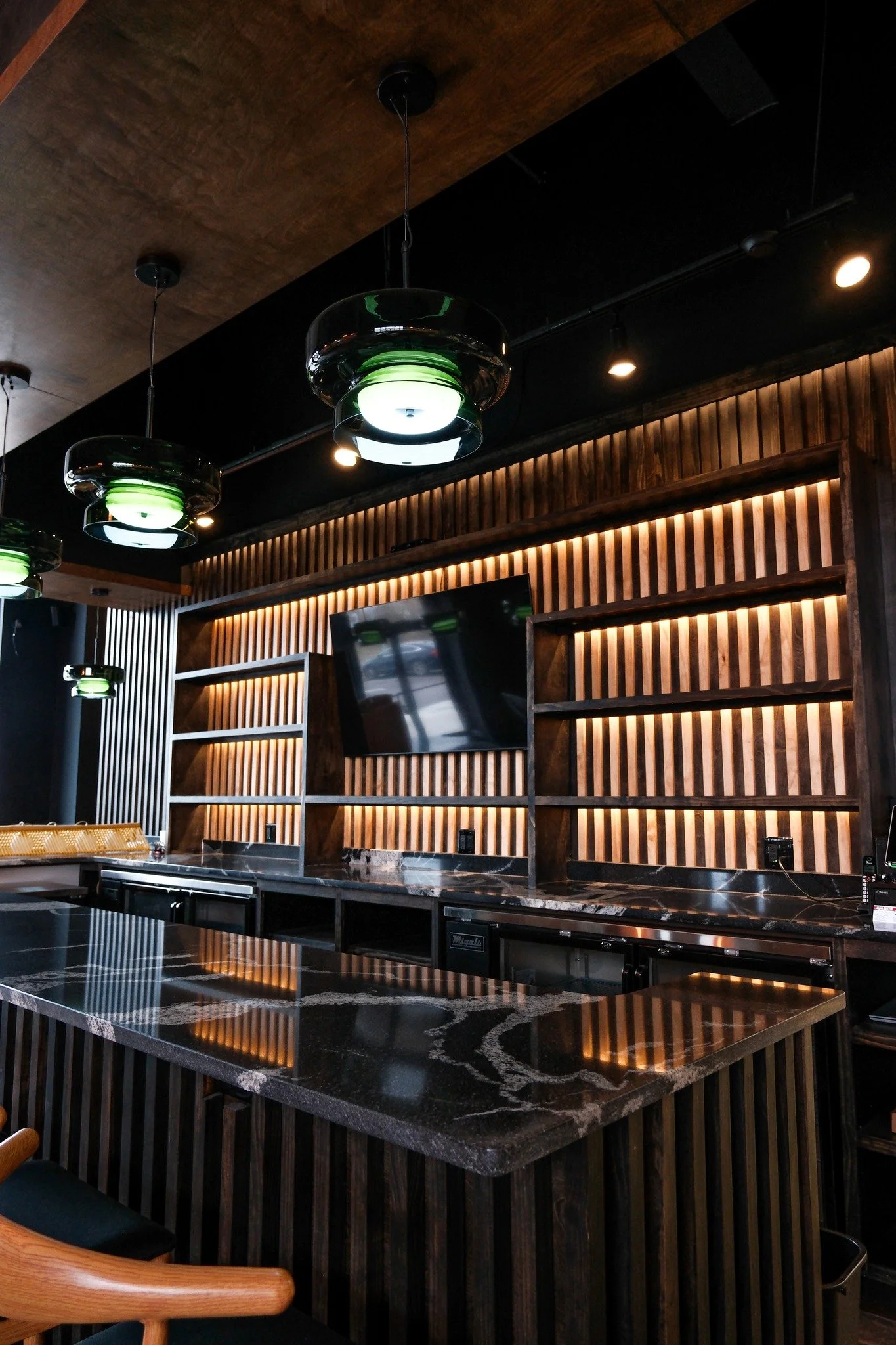 Interior of a modern restaurant or bar with dark wood accents, decorative light fixtures, and a black marble countertop.