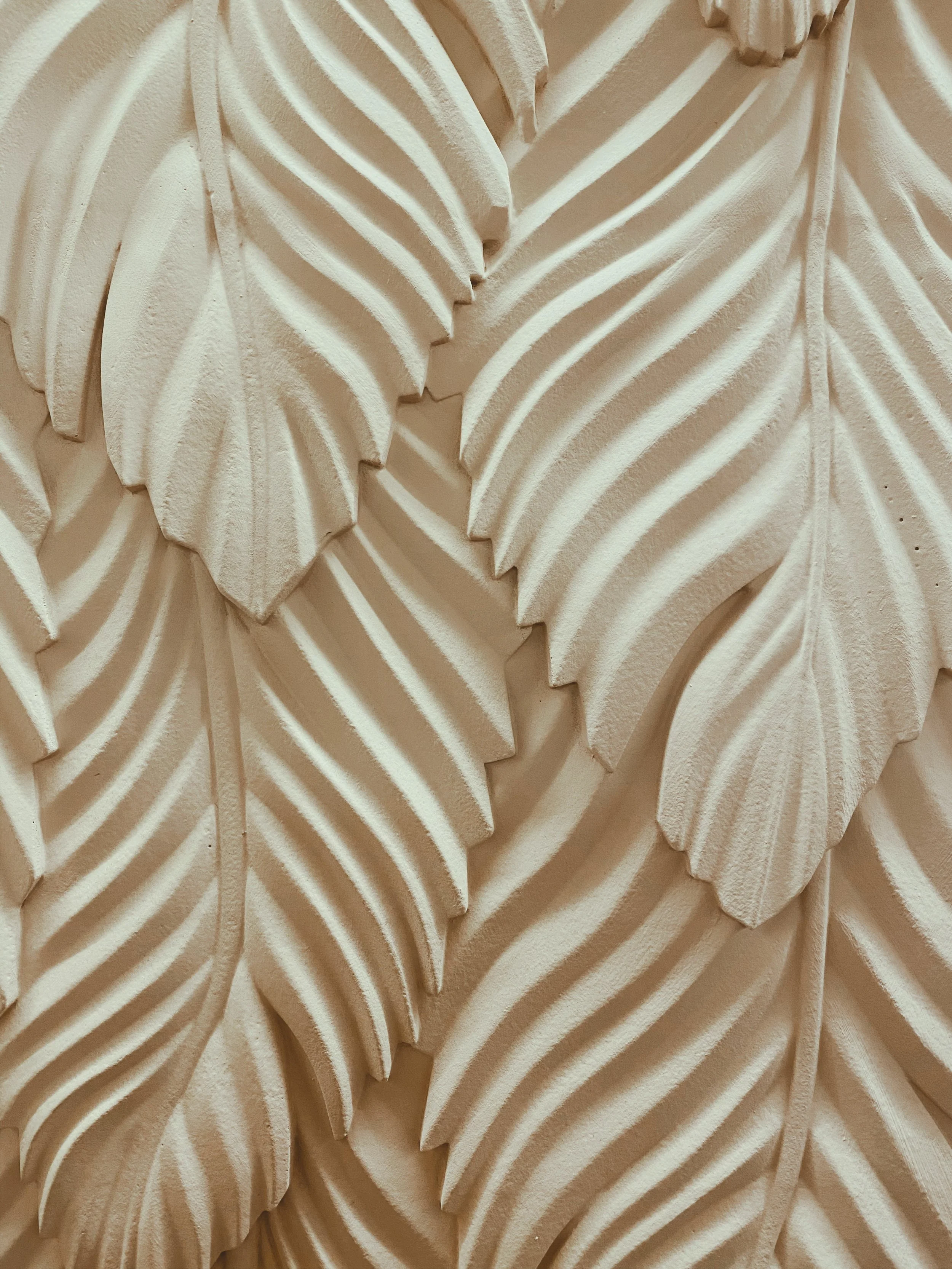 Close-up of a wall decoration with carved, overlapping leaves in a beige or light tan color.