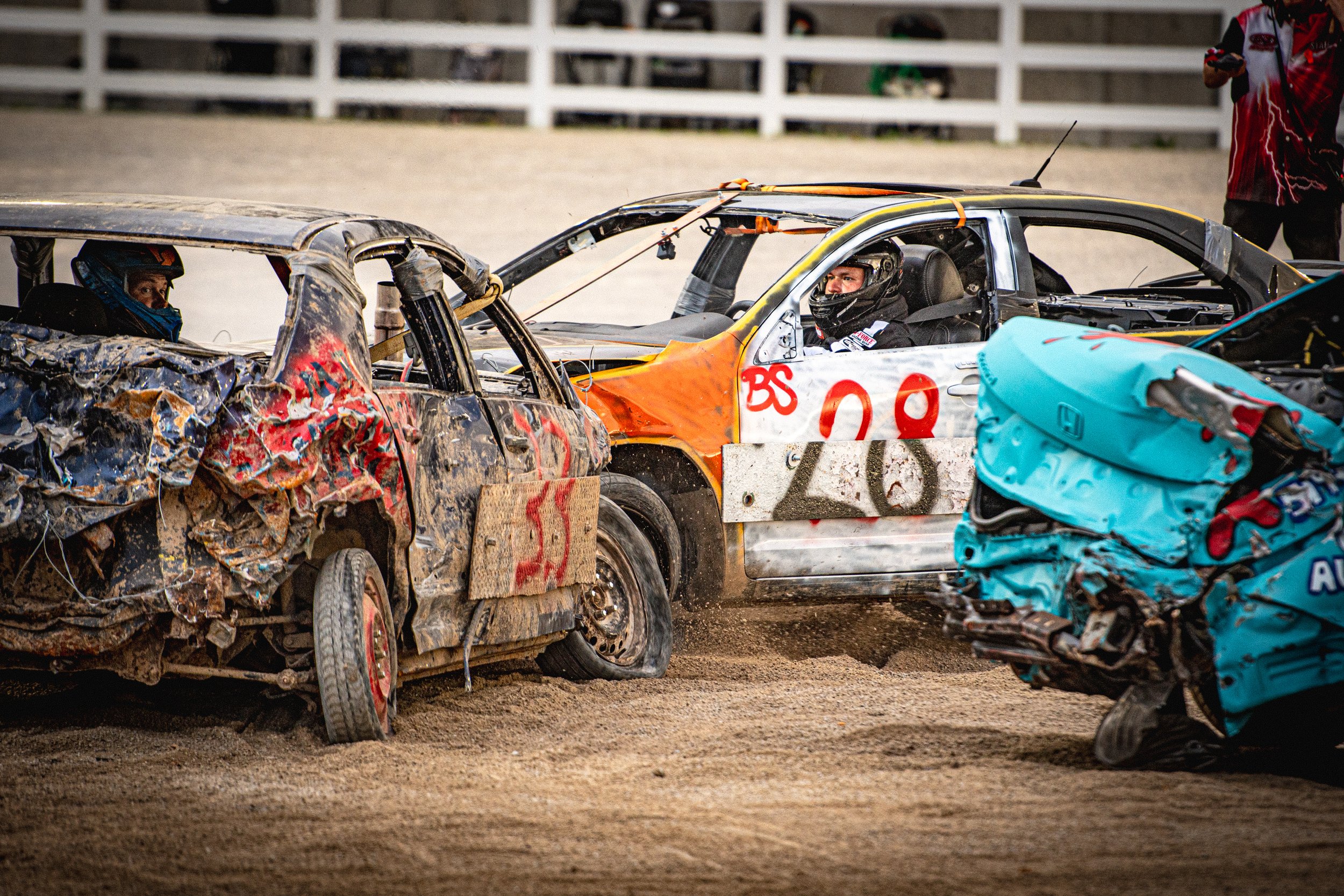 Race cars involved in a crash on a dirt track, with visible damage to the vehicles and drivers wearing helmets.