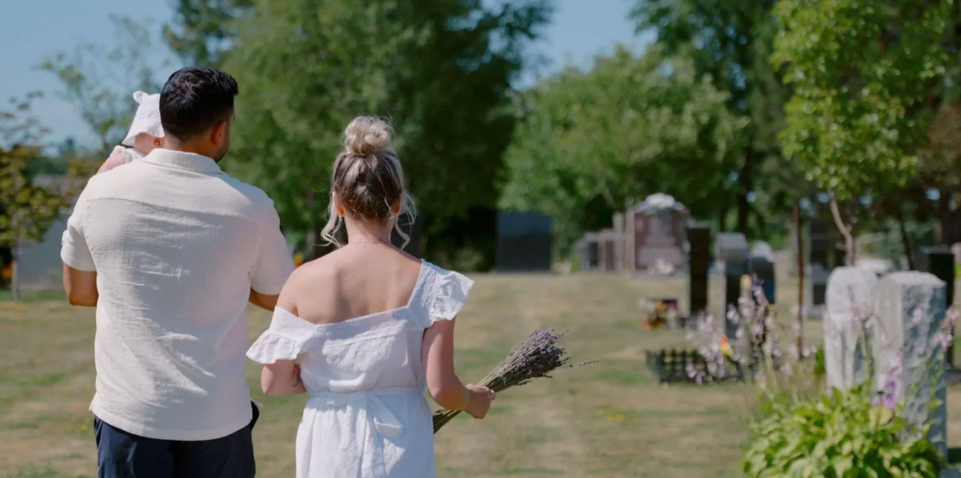 man and woman walking through graveyard holding their daughter and flowers