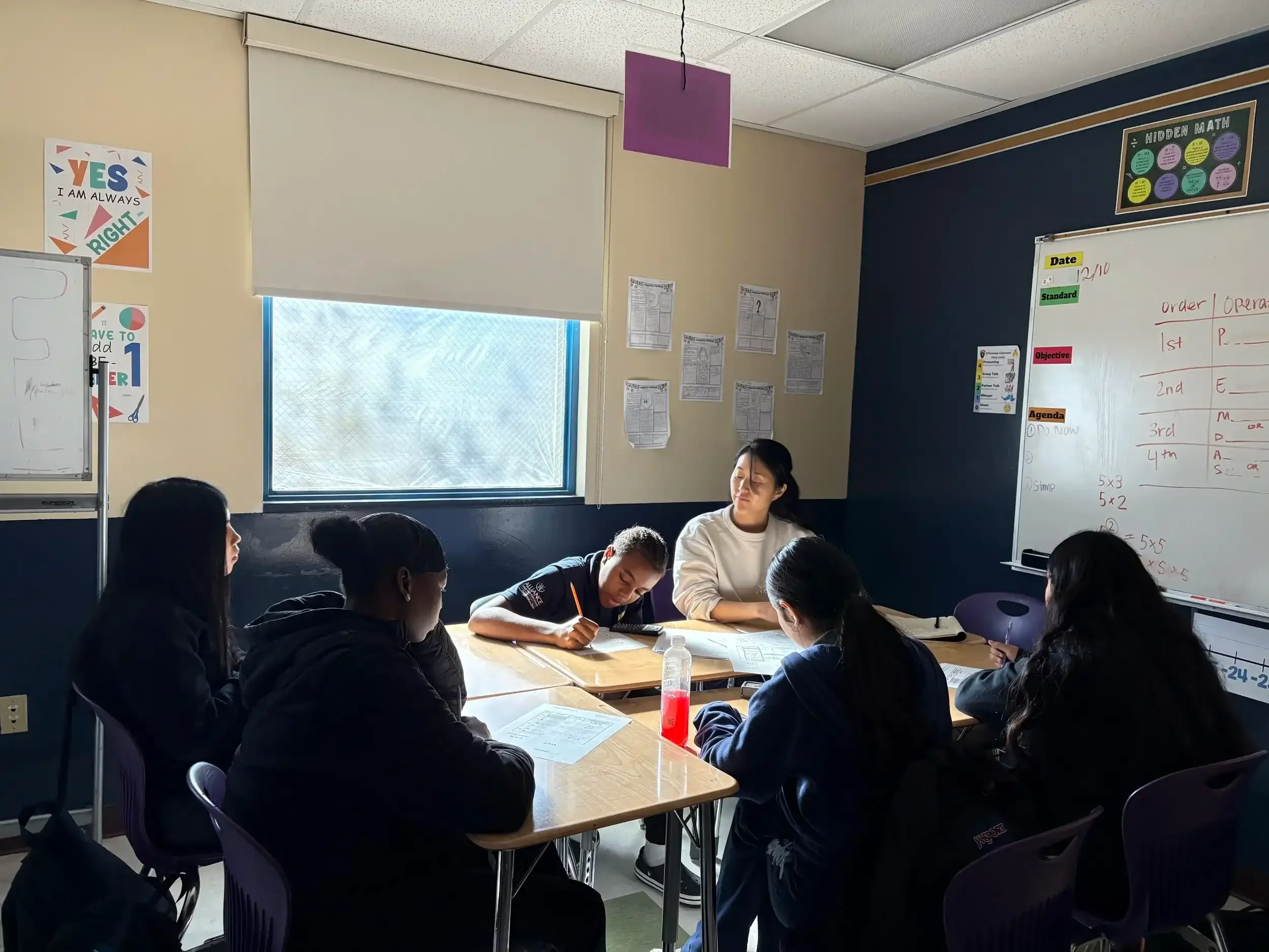 A professional tutor helping middle school students with an in-class math lesson.