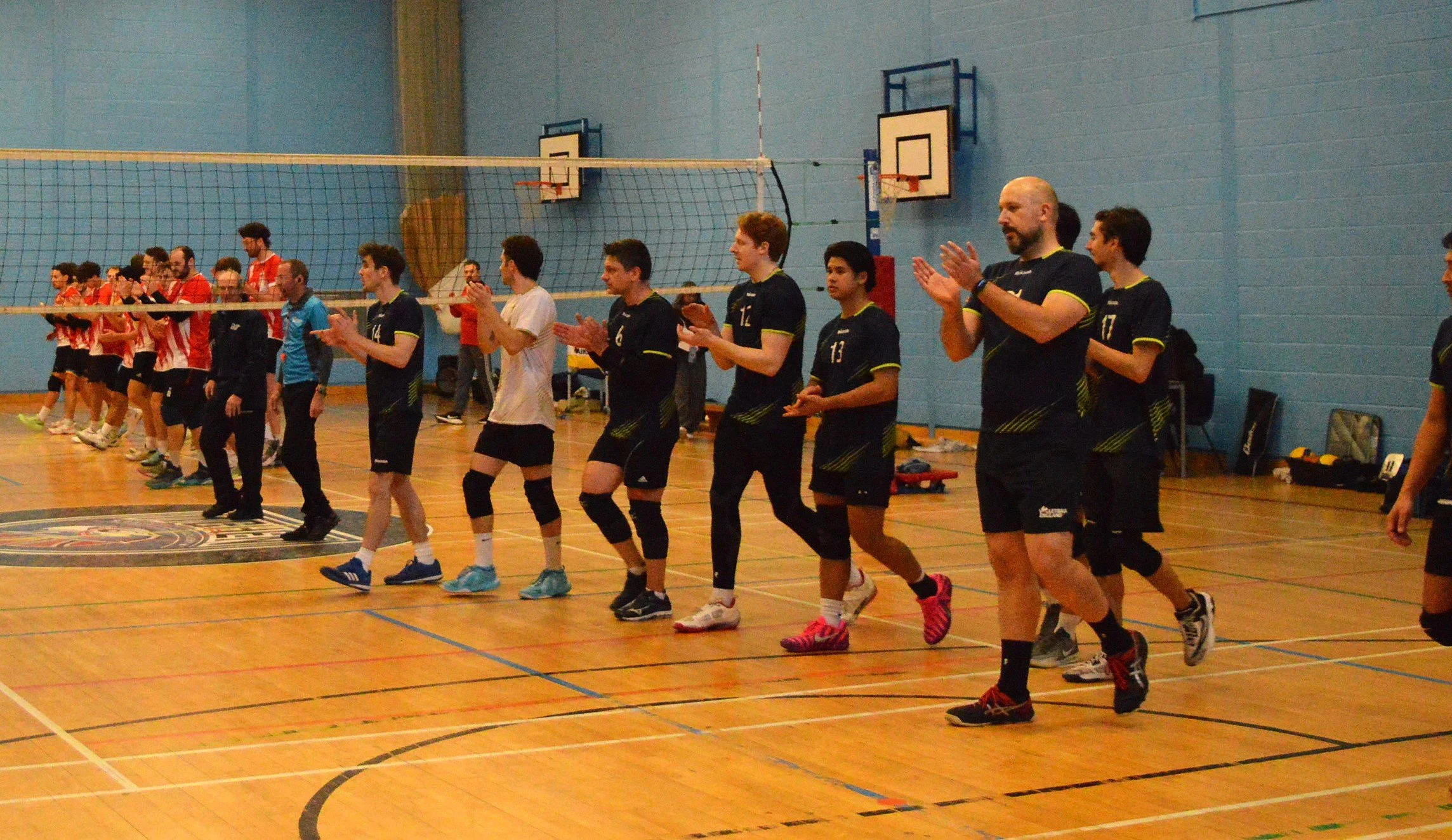 Group of male volleyball players in blue jerseys holding trophies and awards in a gym.