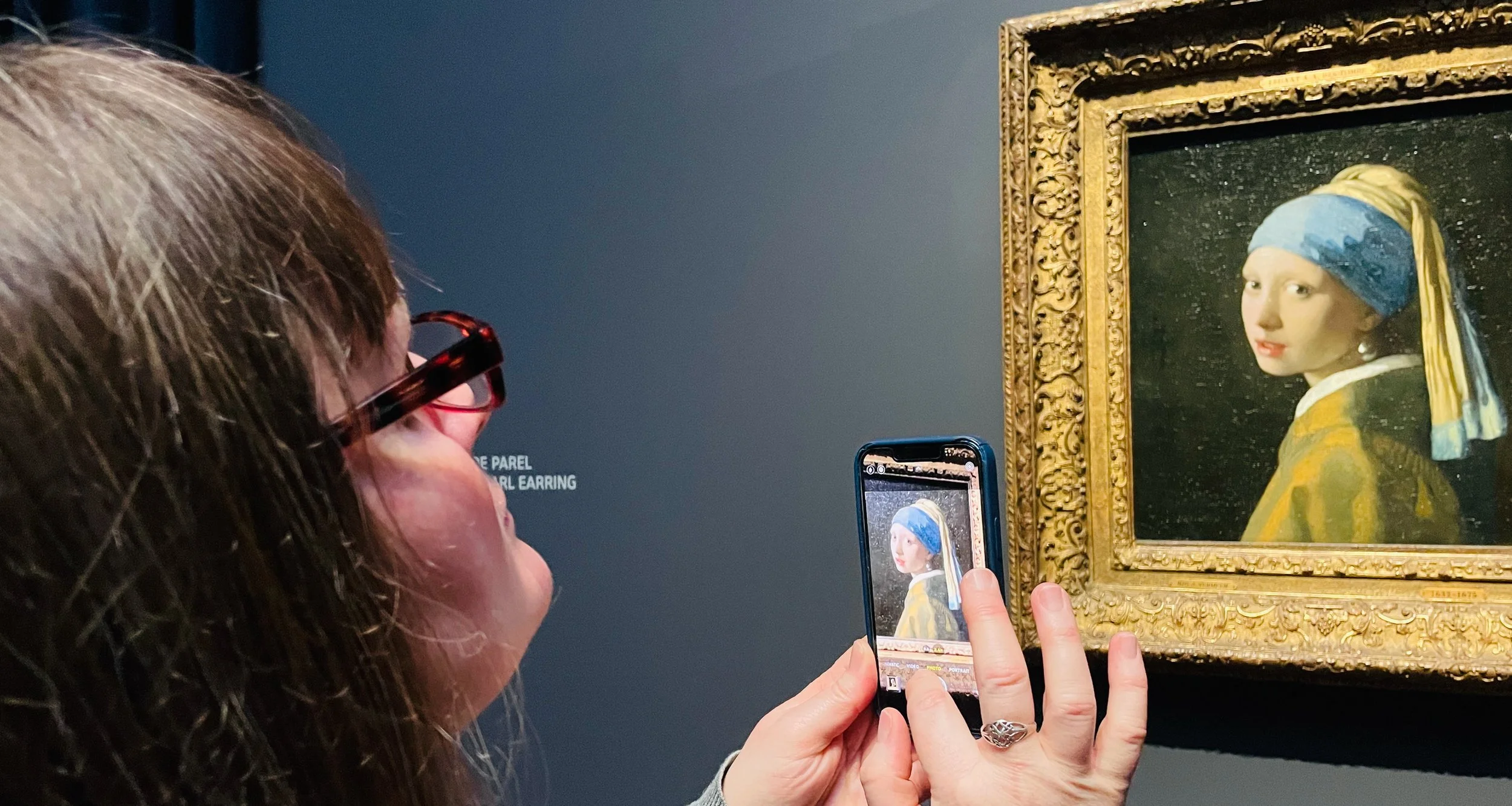 A woman holds up her phone to take a photograph of Vermeer's most famous painting, Girl With a Pearl Earring.